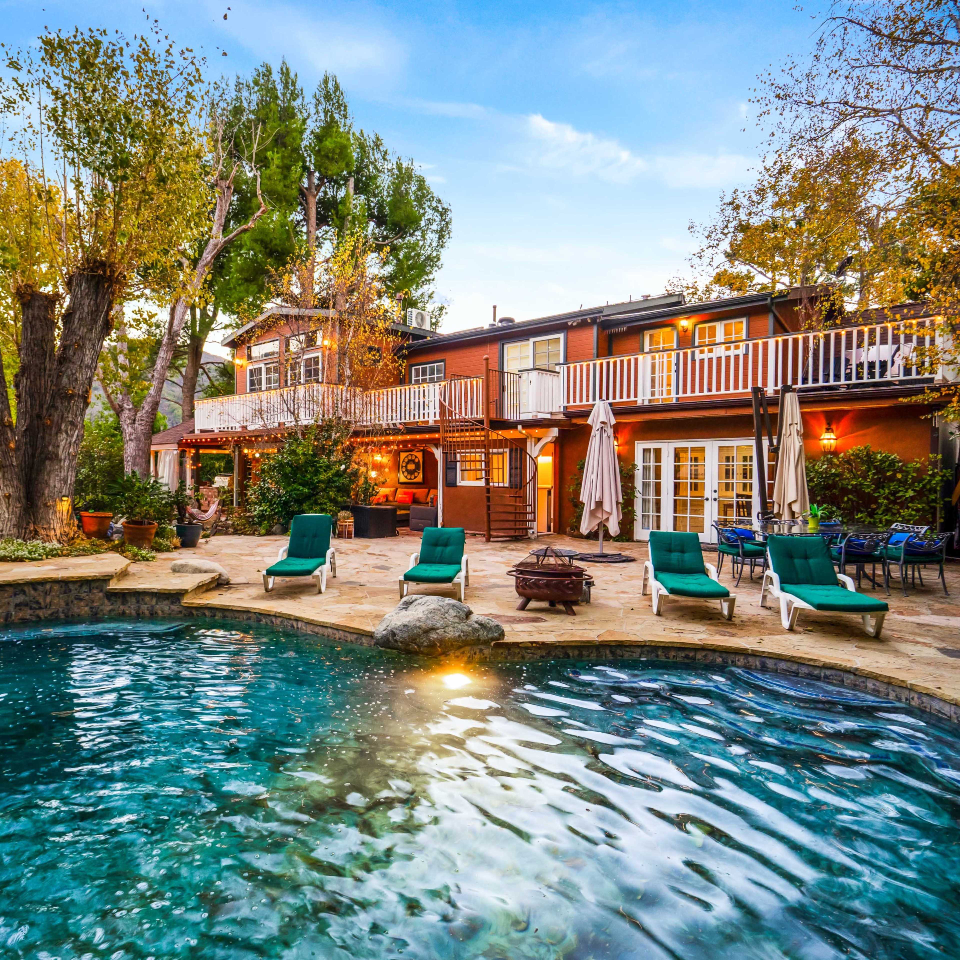 A backyard with a swimming pool, lounge chairs, and a two-story house surrounded by trees.