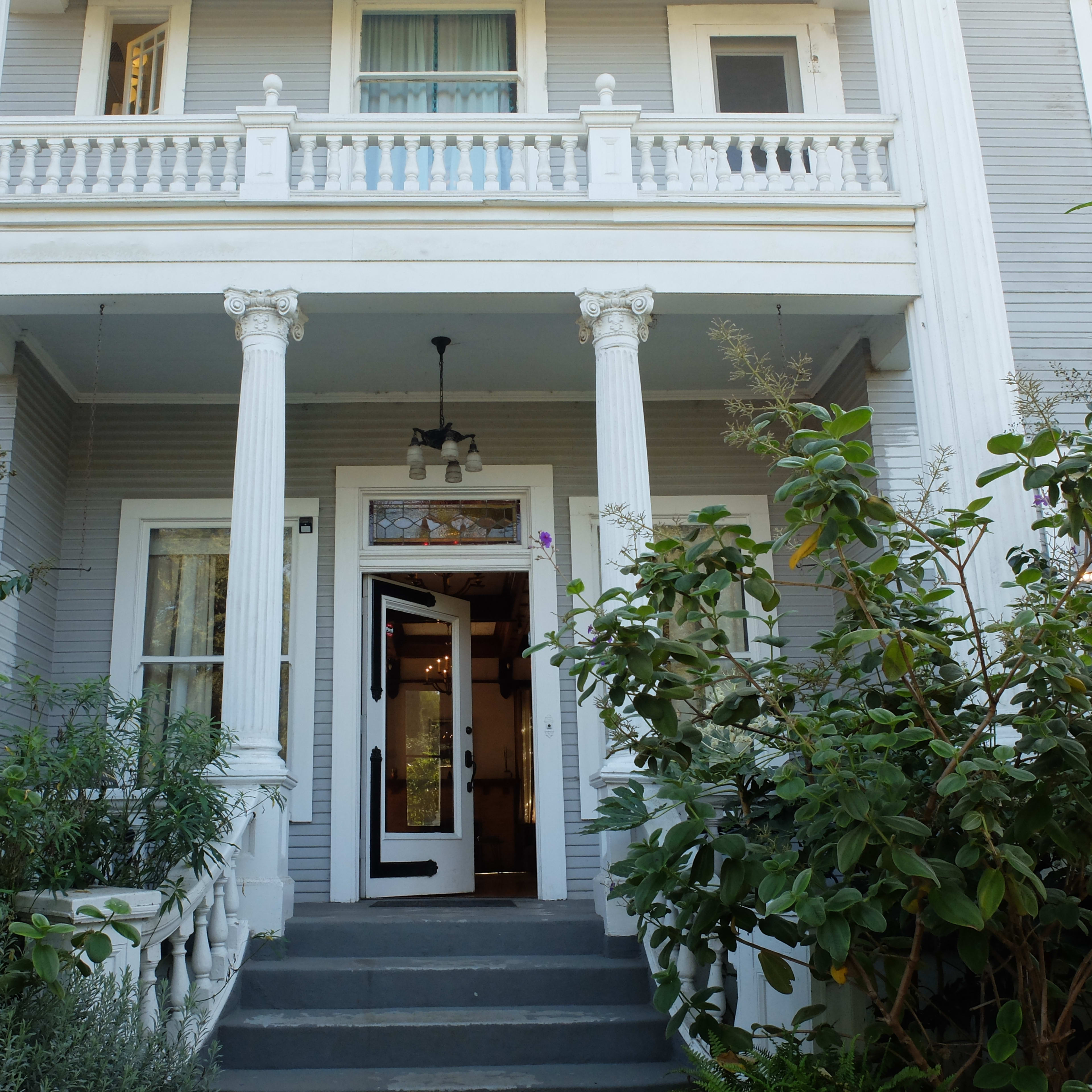 A two-story house with a front porch supported by columns, leading to an open door.