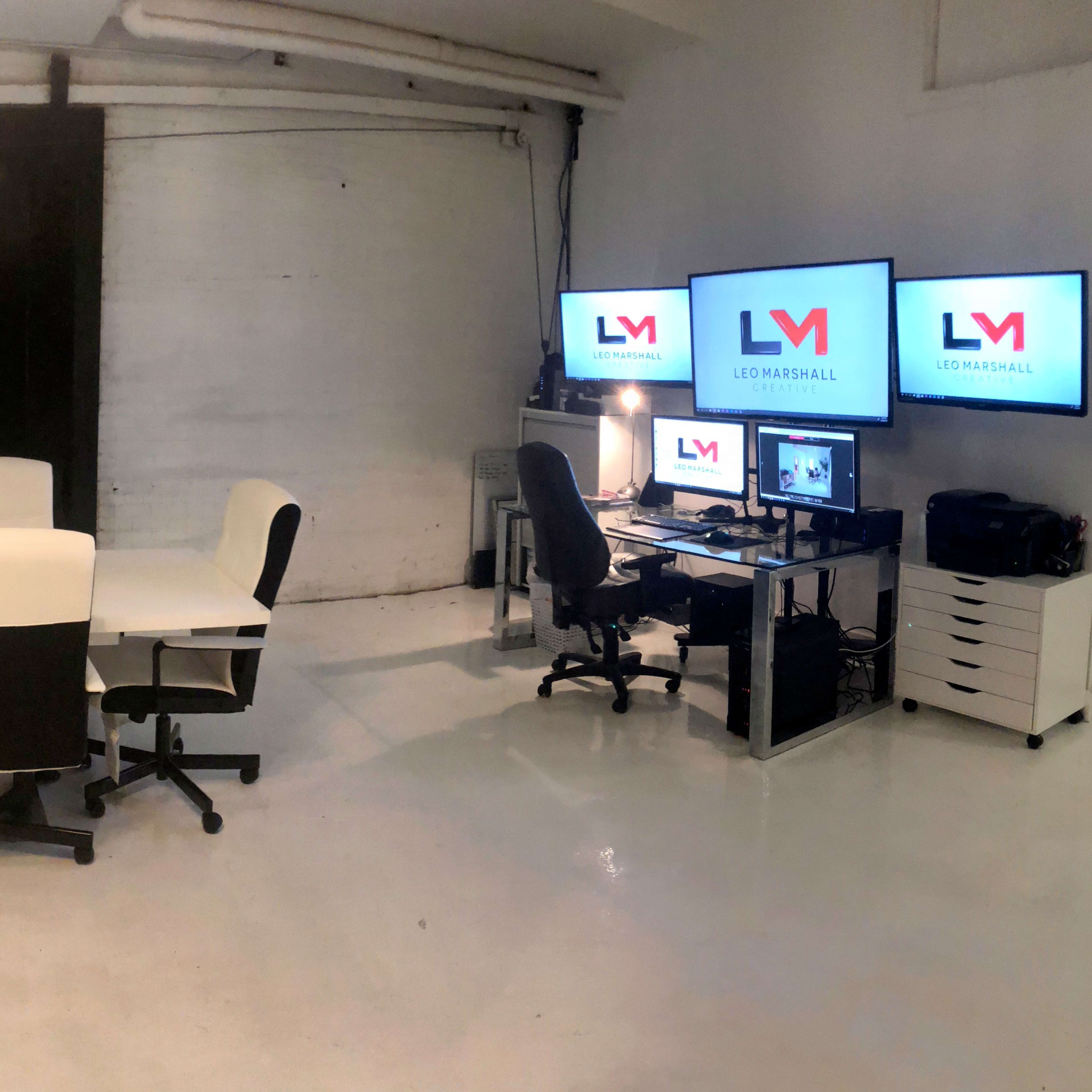 A modern office space featuring a large conference table with six chairs, two computer monitors, and a display screen on one wall.