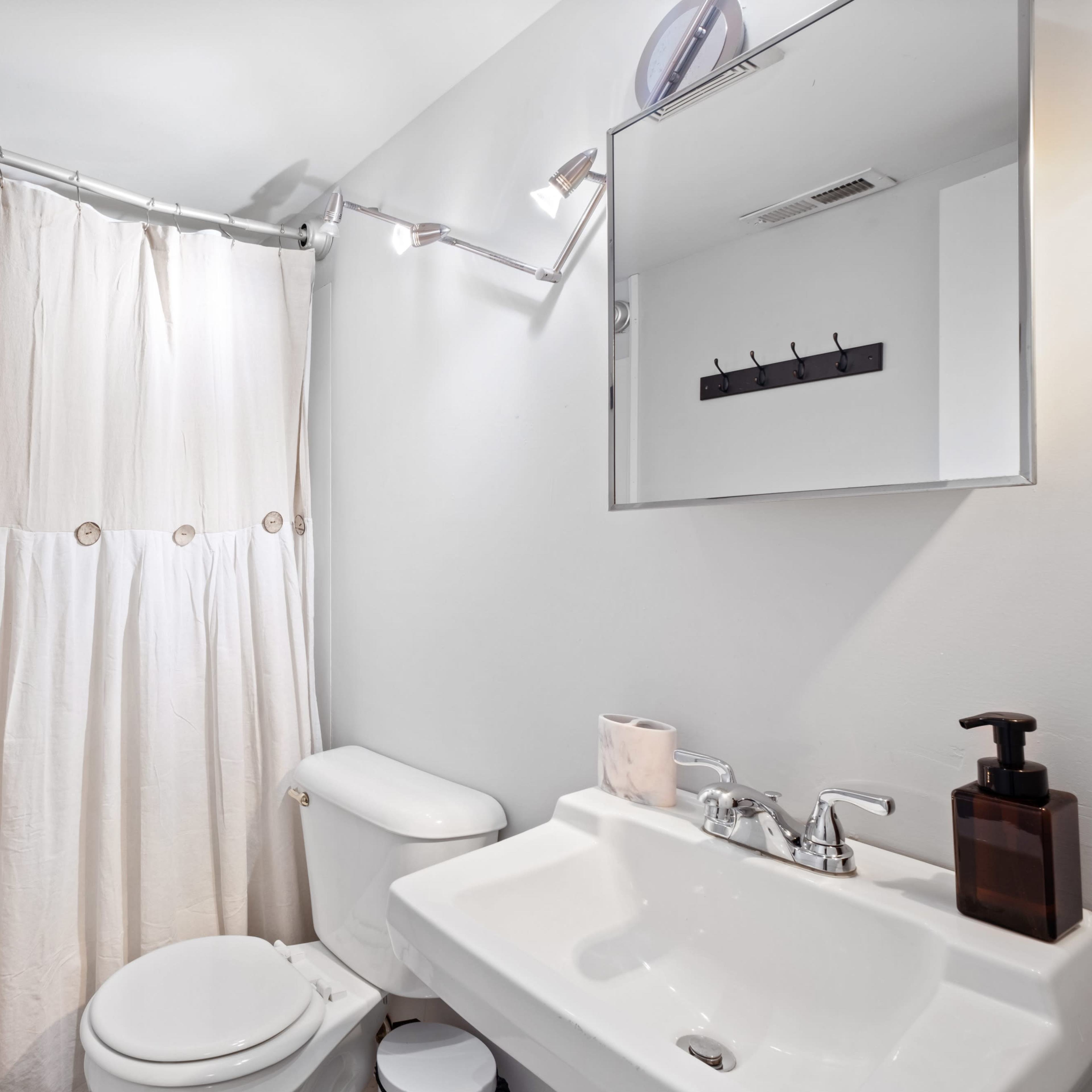 A bathroom with a shower area, a toilet, and a sink, featuring a curtain and a wall-mounted mirror.