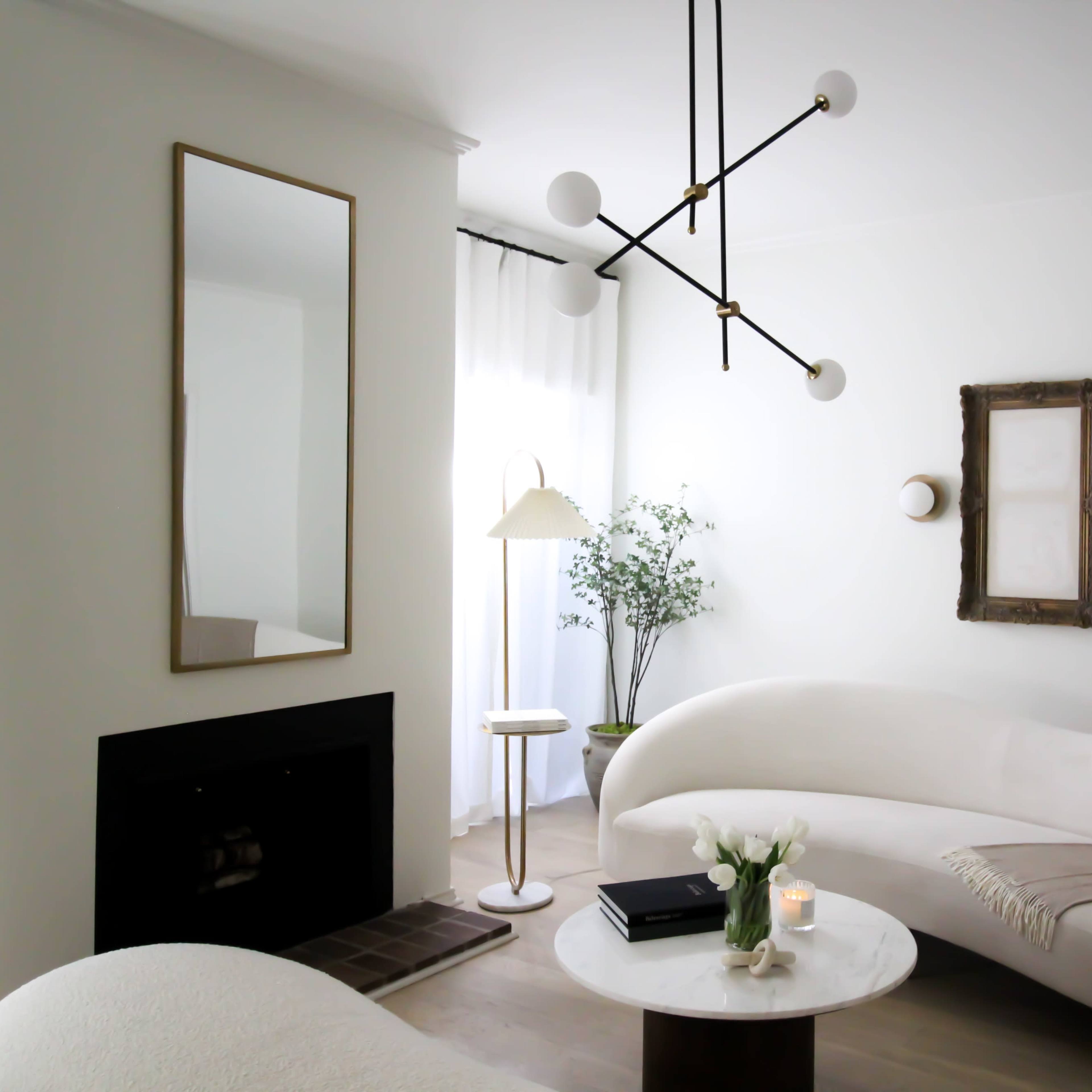 A light, modern living room with a curved sofa, a round coffee table, and a floor lamp, accompanied by decorative elements and a minimalist aesthetic.