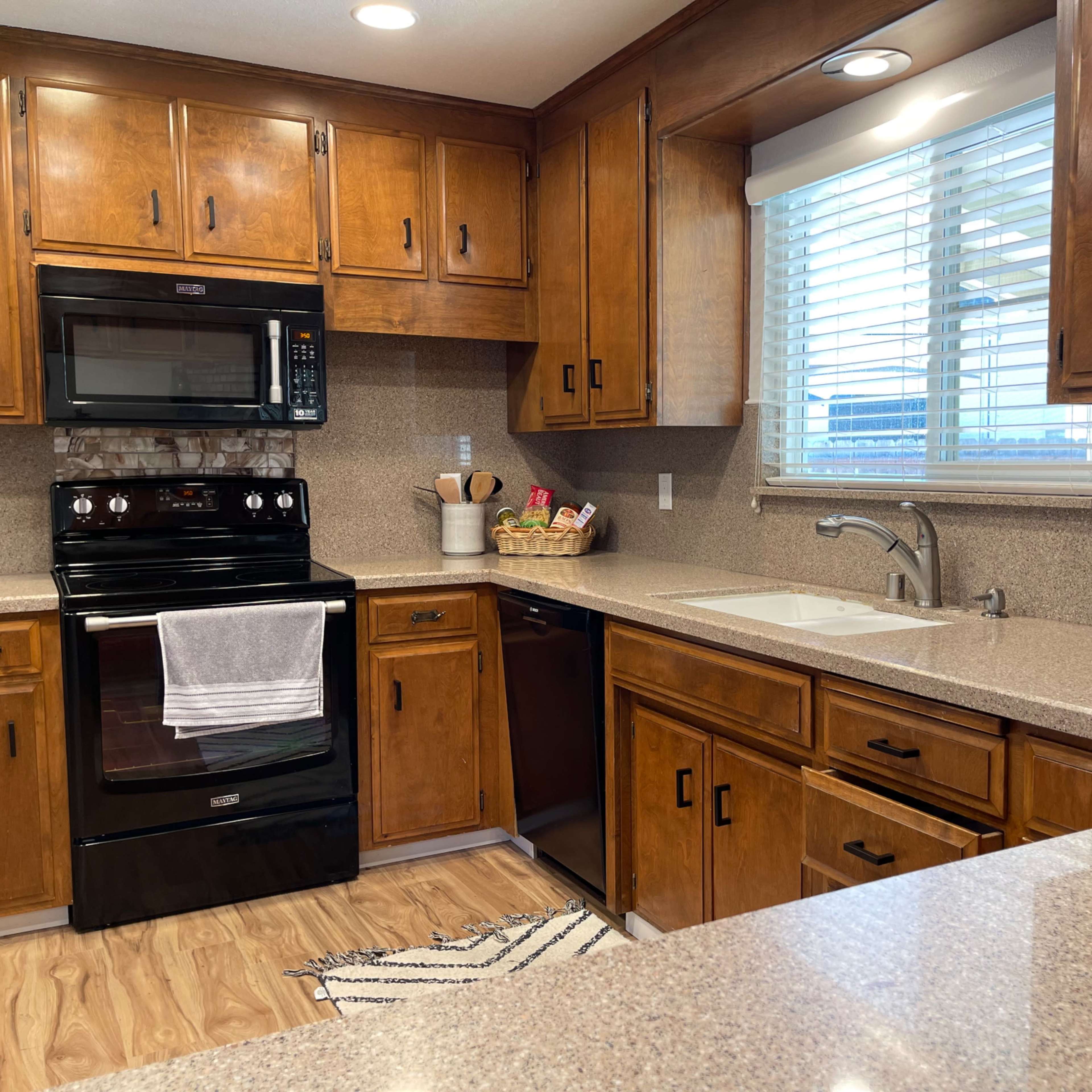 A kitchen with wooden cabinets, black appliances, and a double sink beside a window with blinds.