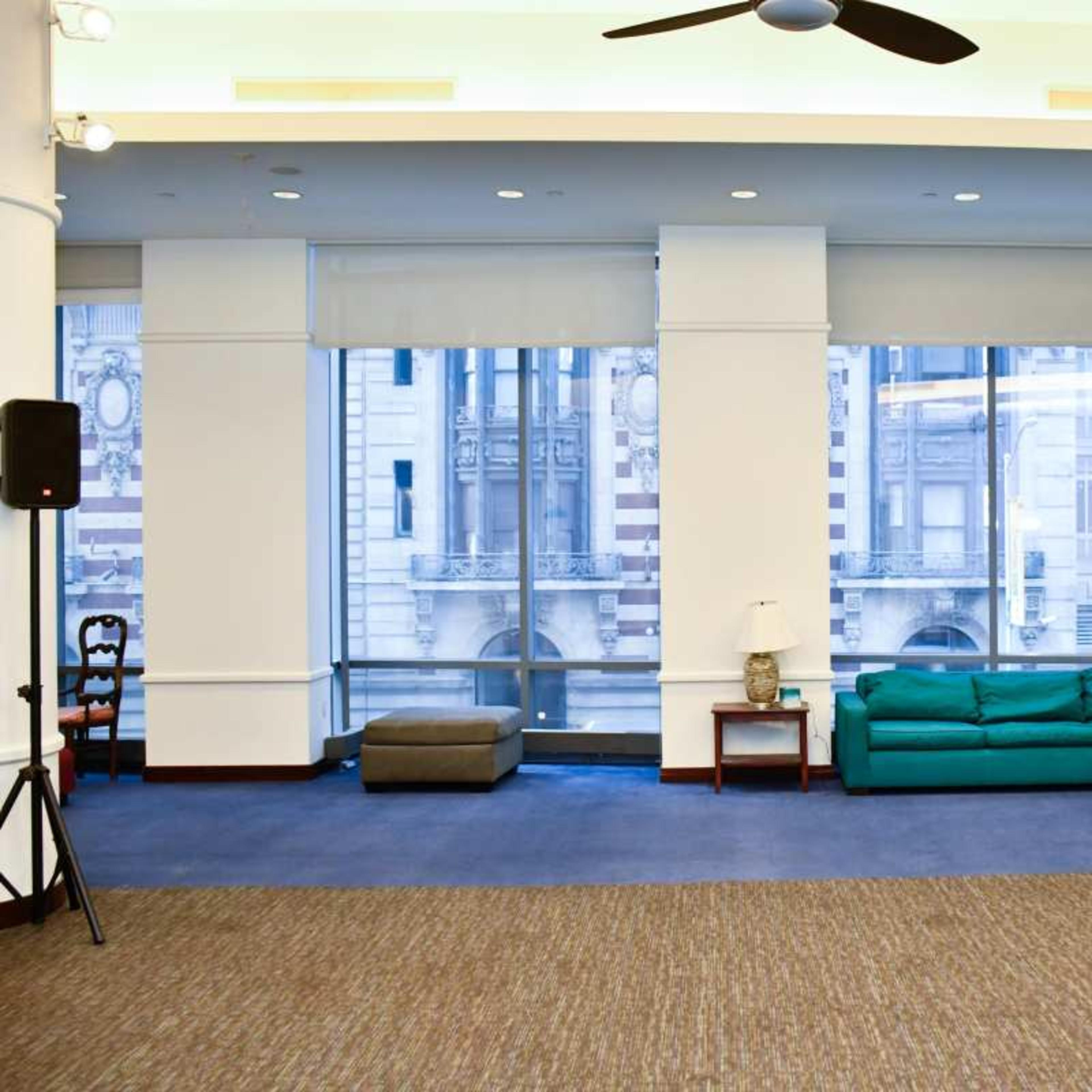 A spacious interior with a green couch, a small wooden table, and large windows displaying a cityscape outside.
