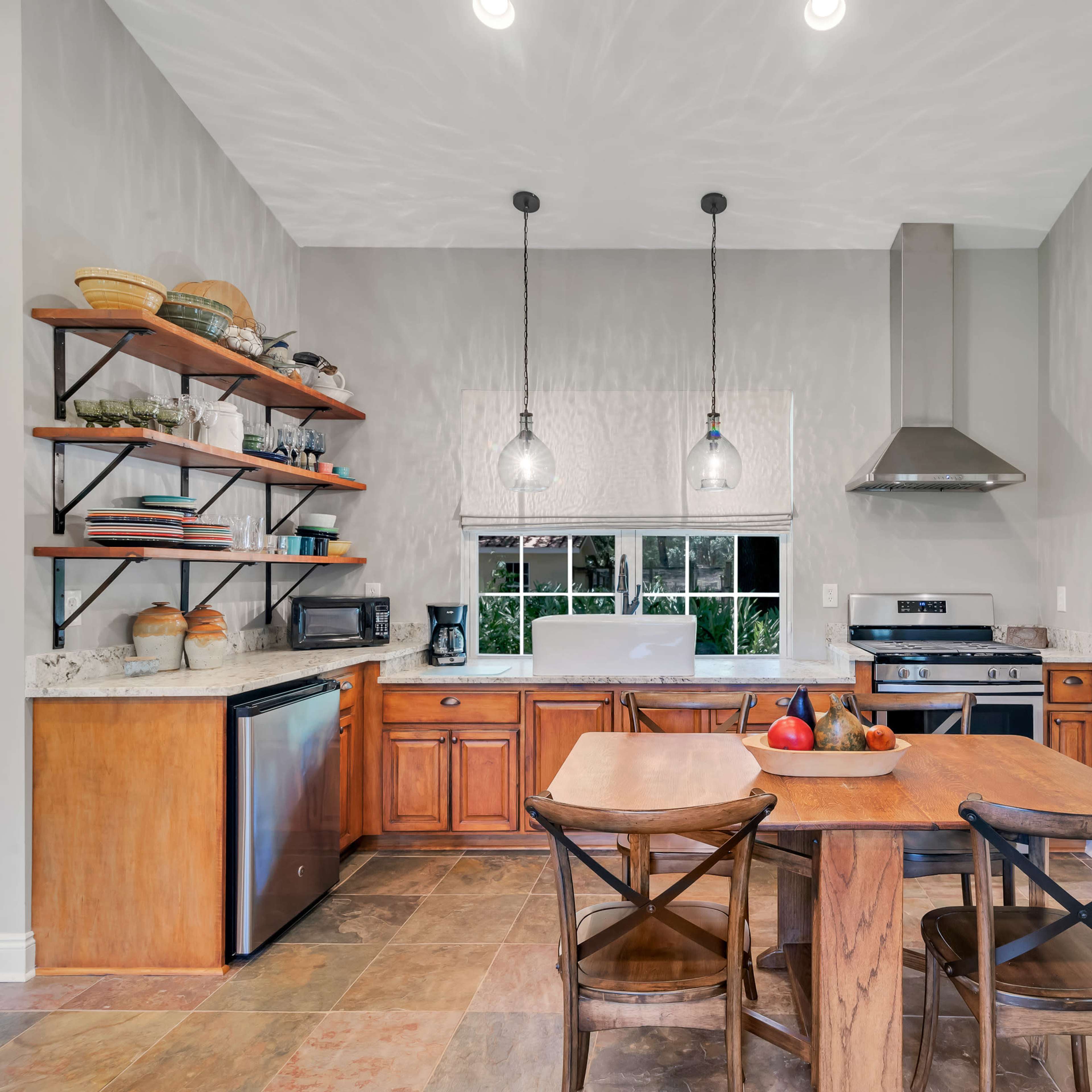 A well-organized kitchen features wooden cabinets, a stainless steel stove, and a dining table with chairs, illuminated by pendant lights.