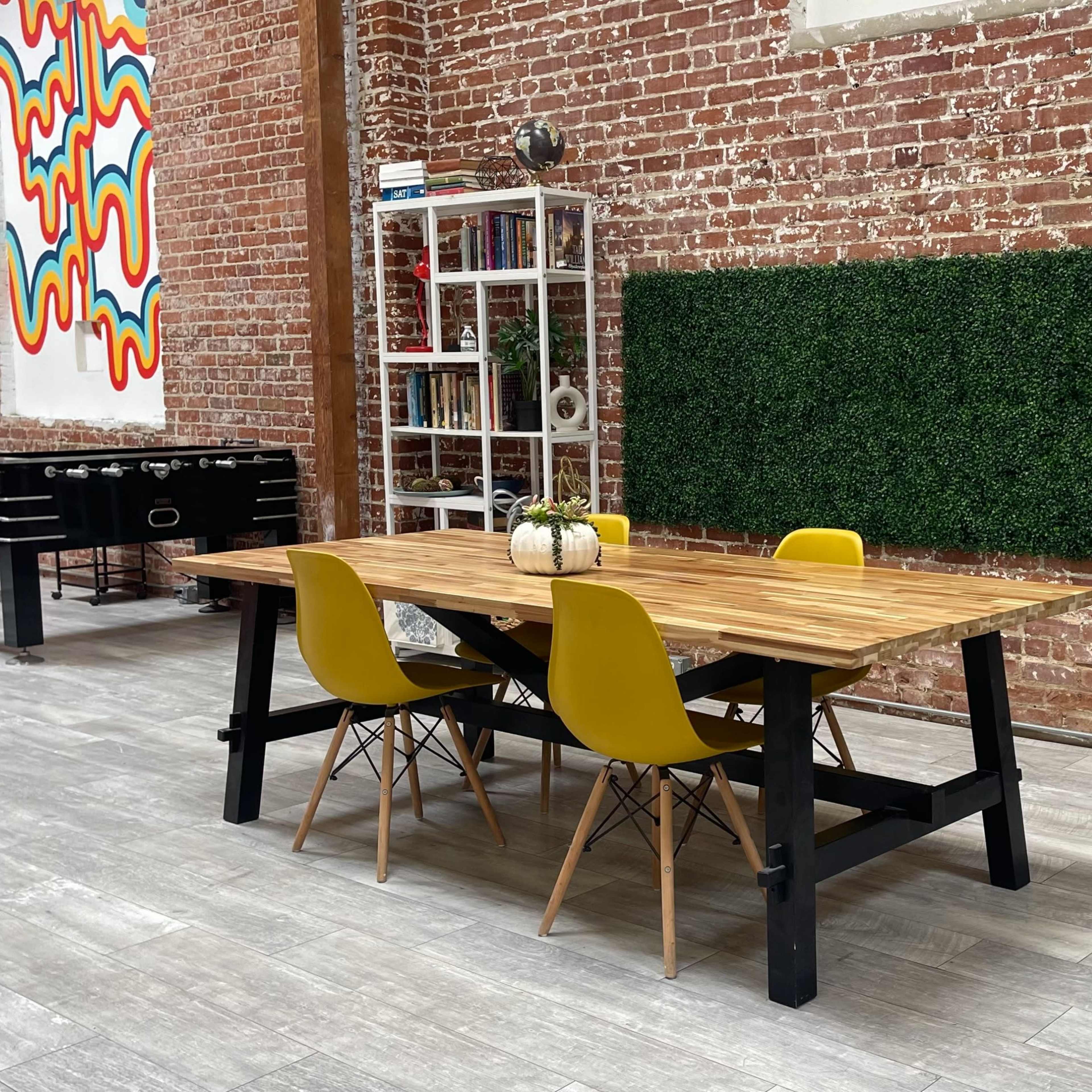 A wooden dining table with yellow chairs is positioned on tile flooring in a spacious room featuring exposed brick walls and decorative elements.