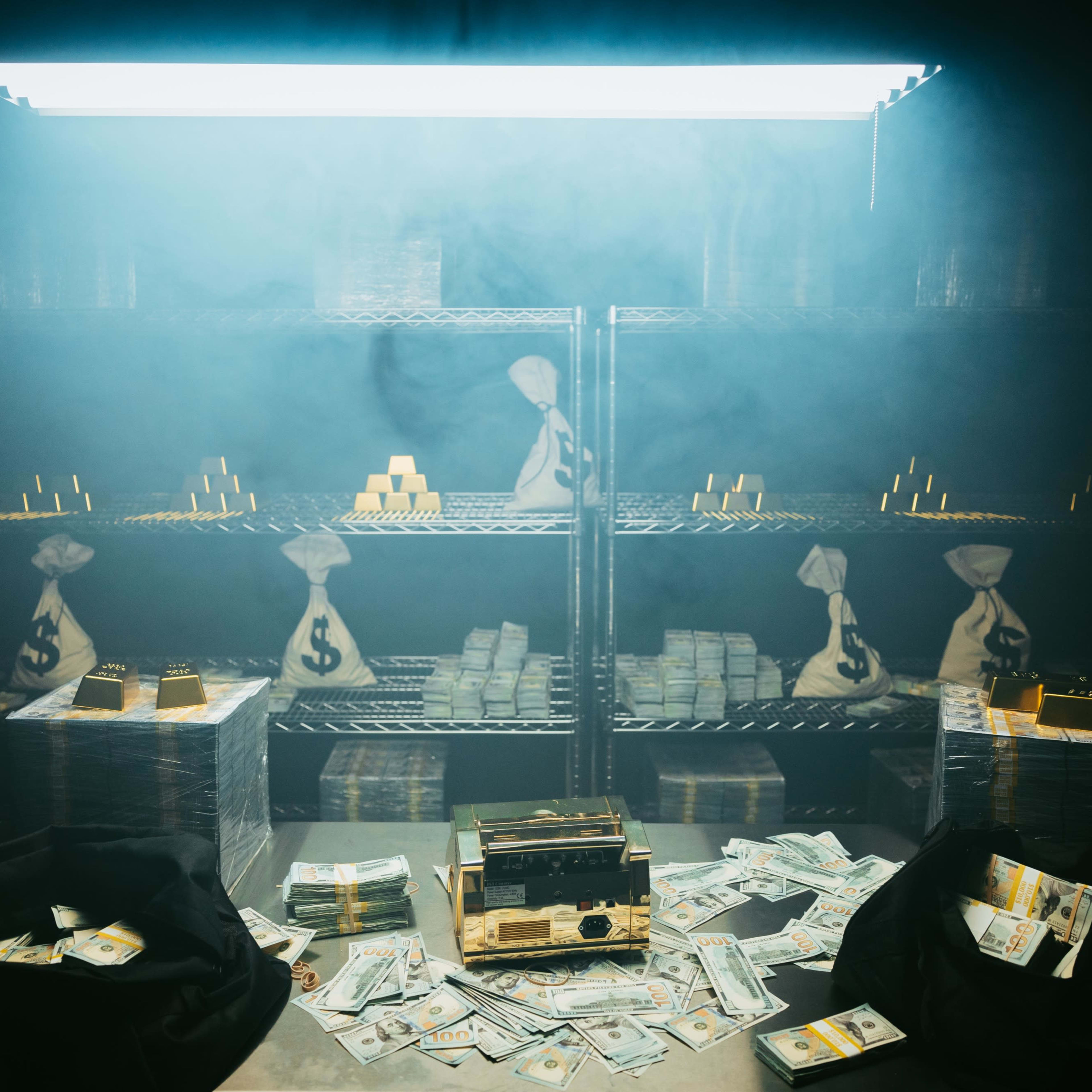 The scene features shelves filled with stacks of cash, bags marked with dollar signs, and gold bars, all shrouded in a foggy atmosphere.