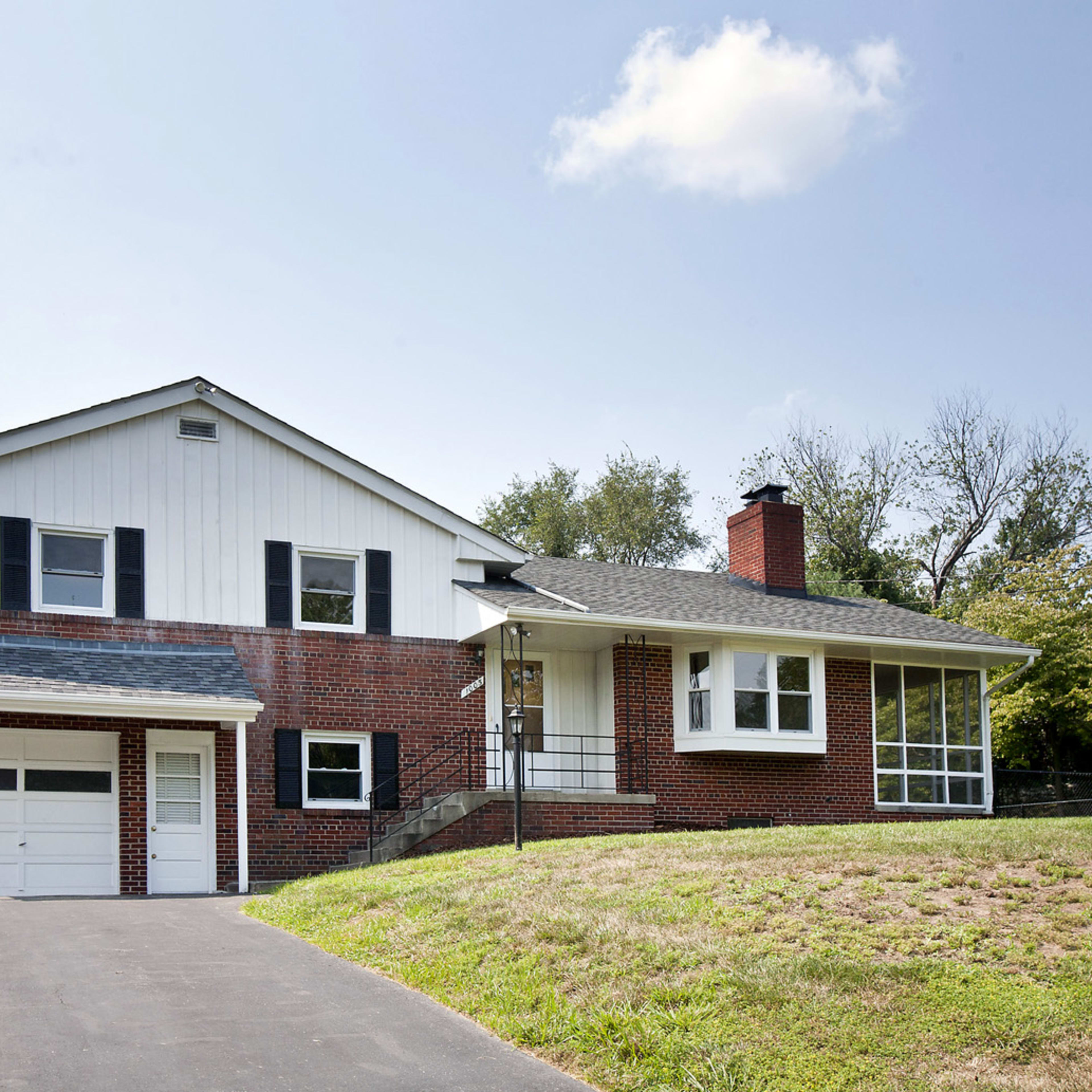 A two-story brick house with a front porch and a garage is situated on a grassy lot.