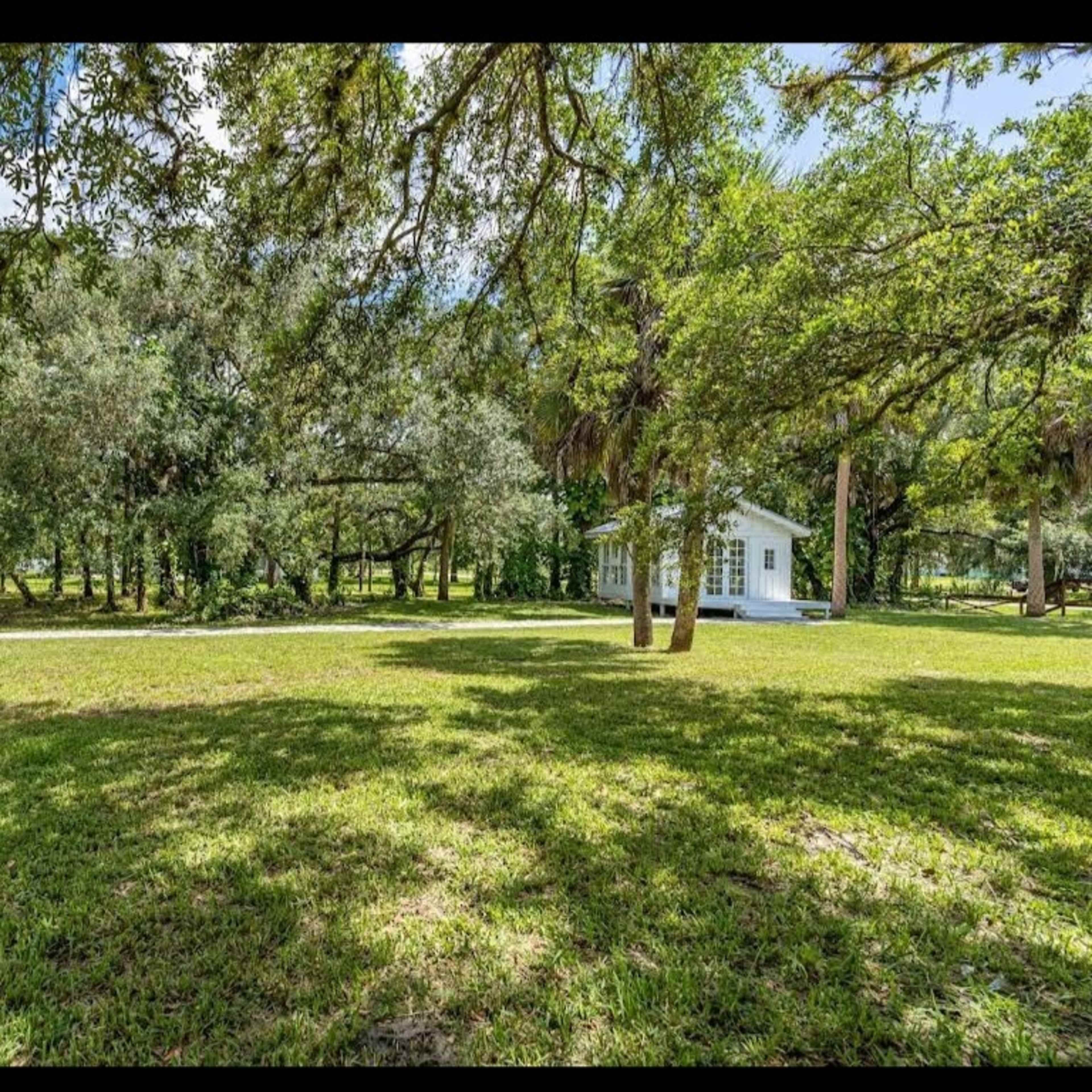 A grassy area surrounded by trees with a white building in the distance.