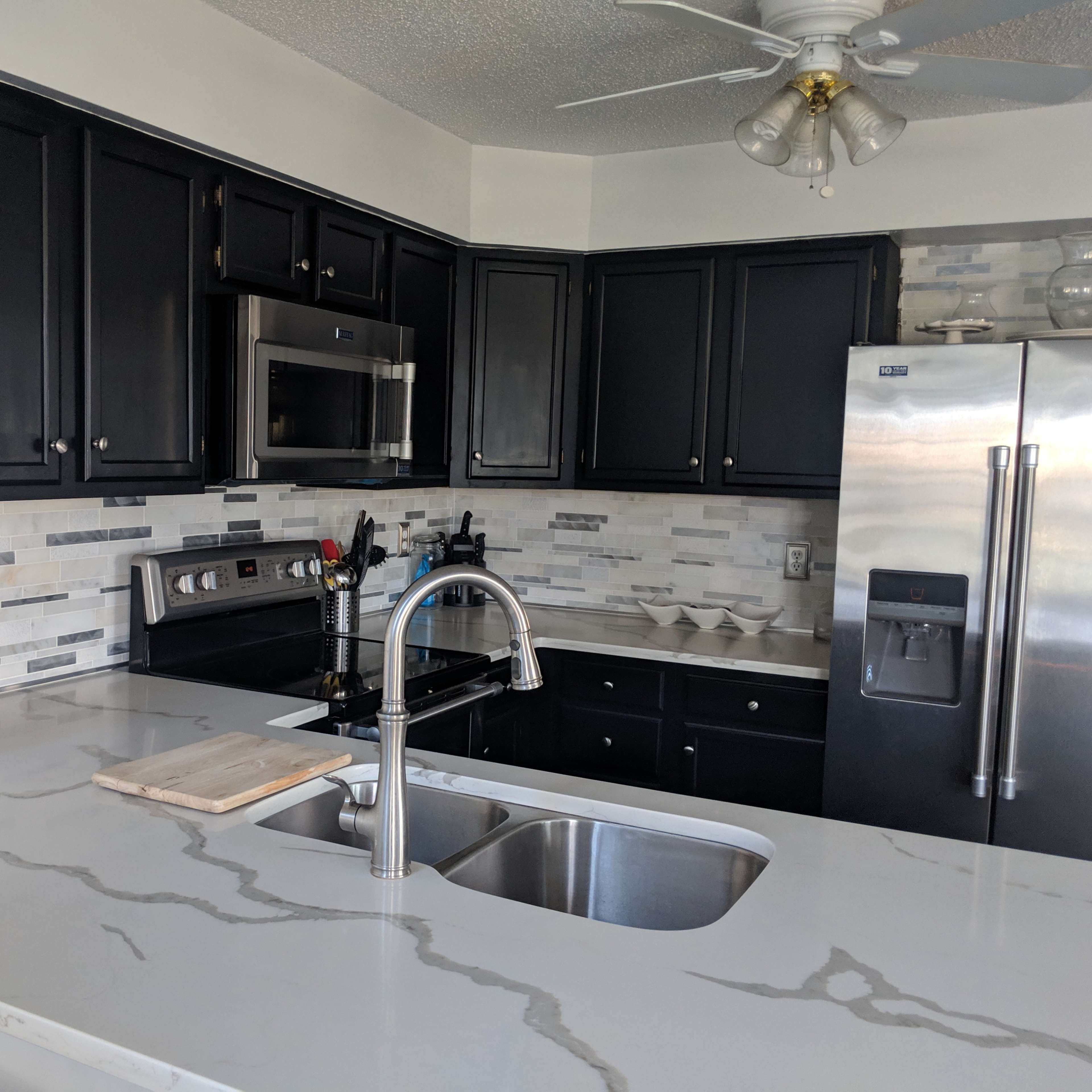 A kitchen with dark cabinets, stainless steel appliances, and a marble countertop featuring a double sink.