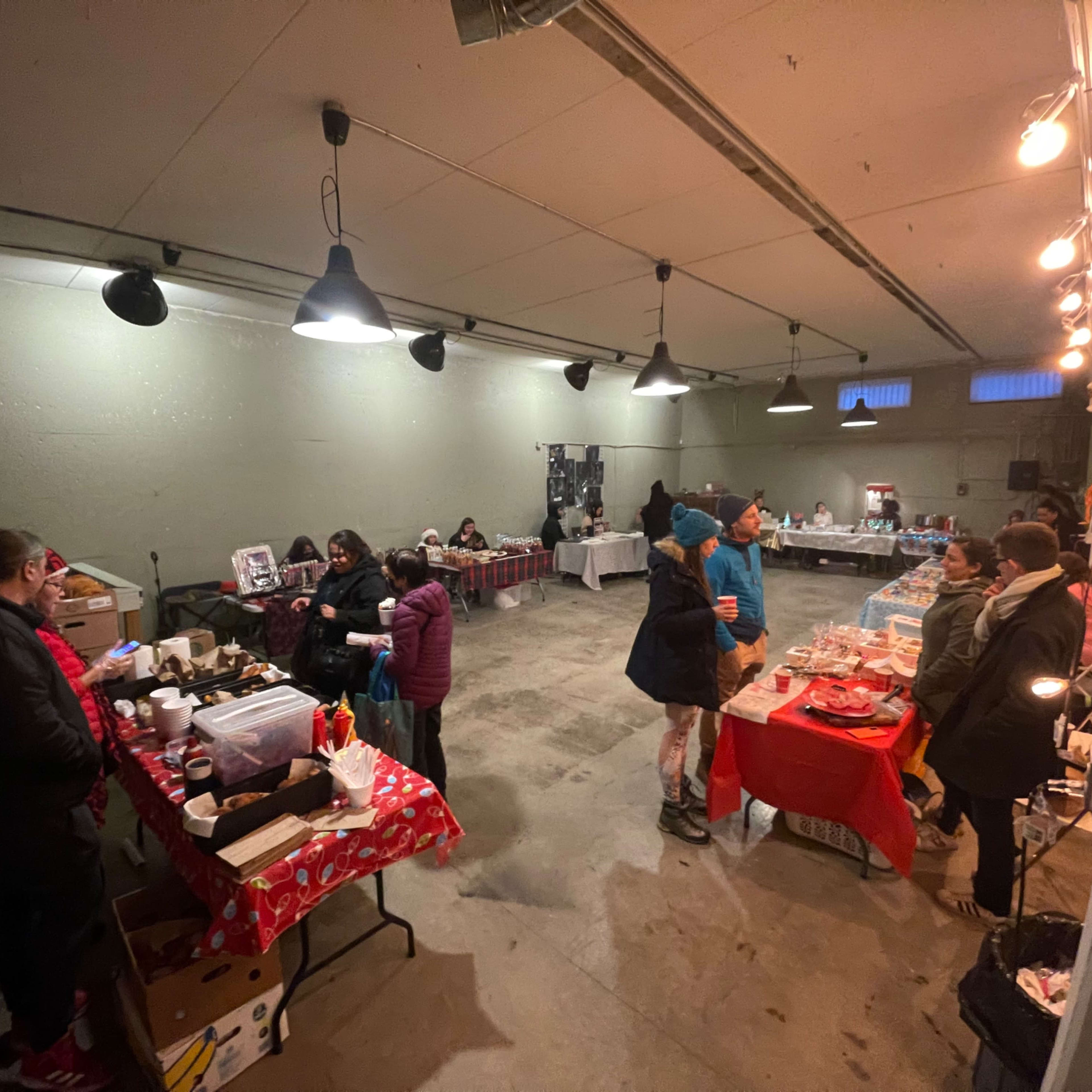 A spacious indoor market scene shows various vendors and customers engaged in activities at tables adorned with red tablecloths.
