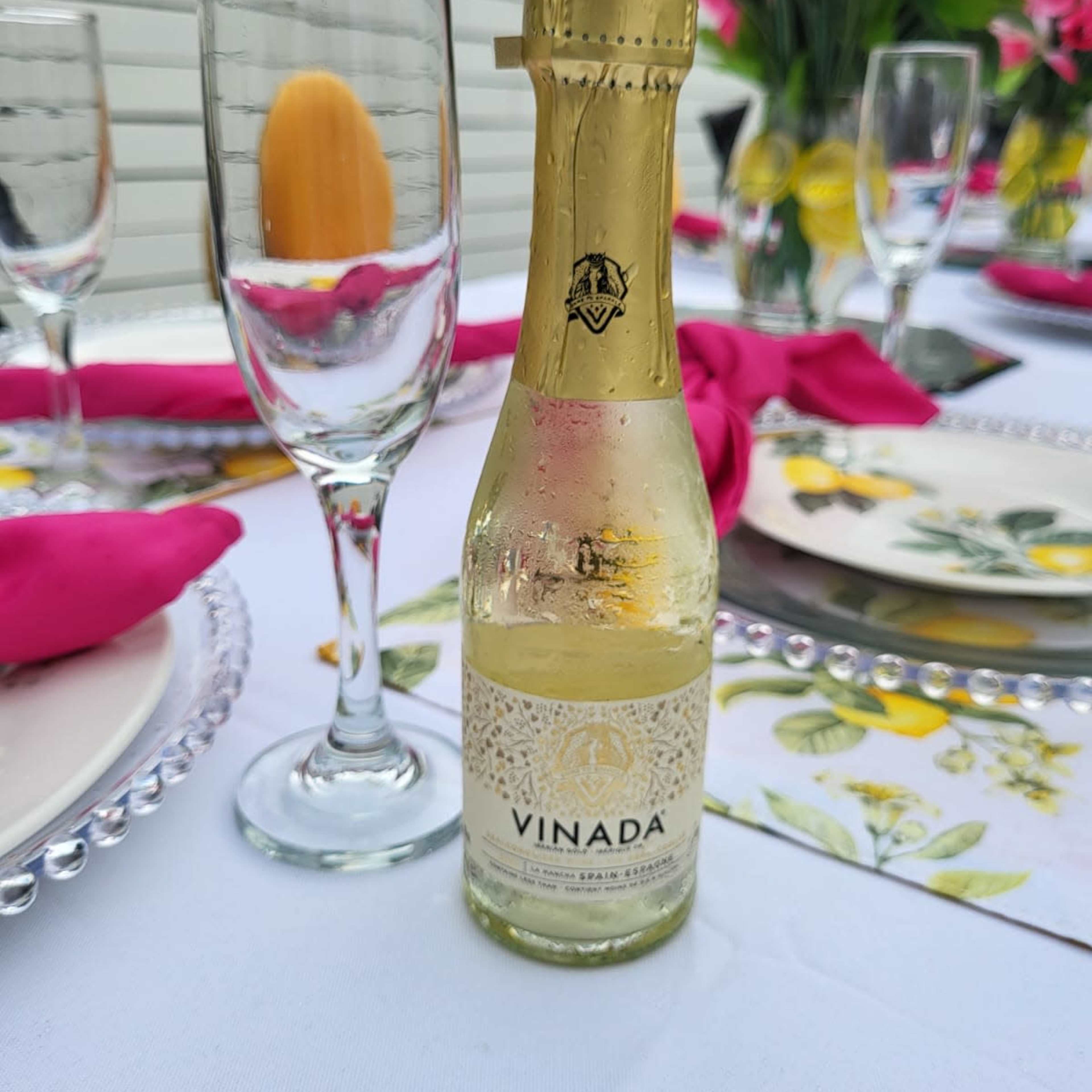 A small bottle of Vinada sparkling wine is placed on a table set with floral arrangements and decorative dinnerware.