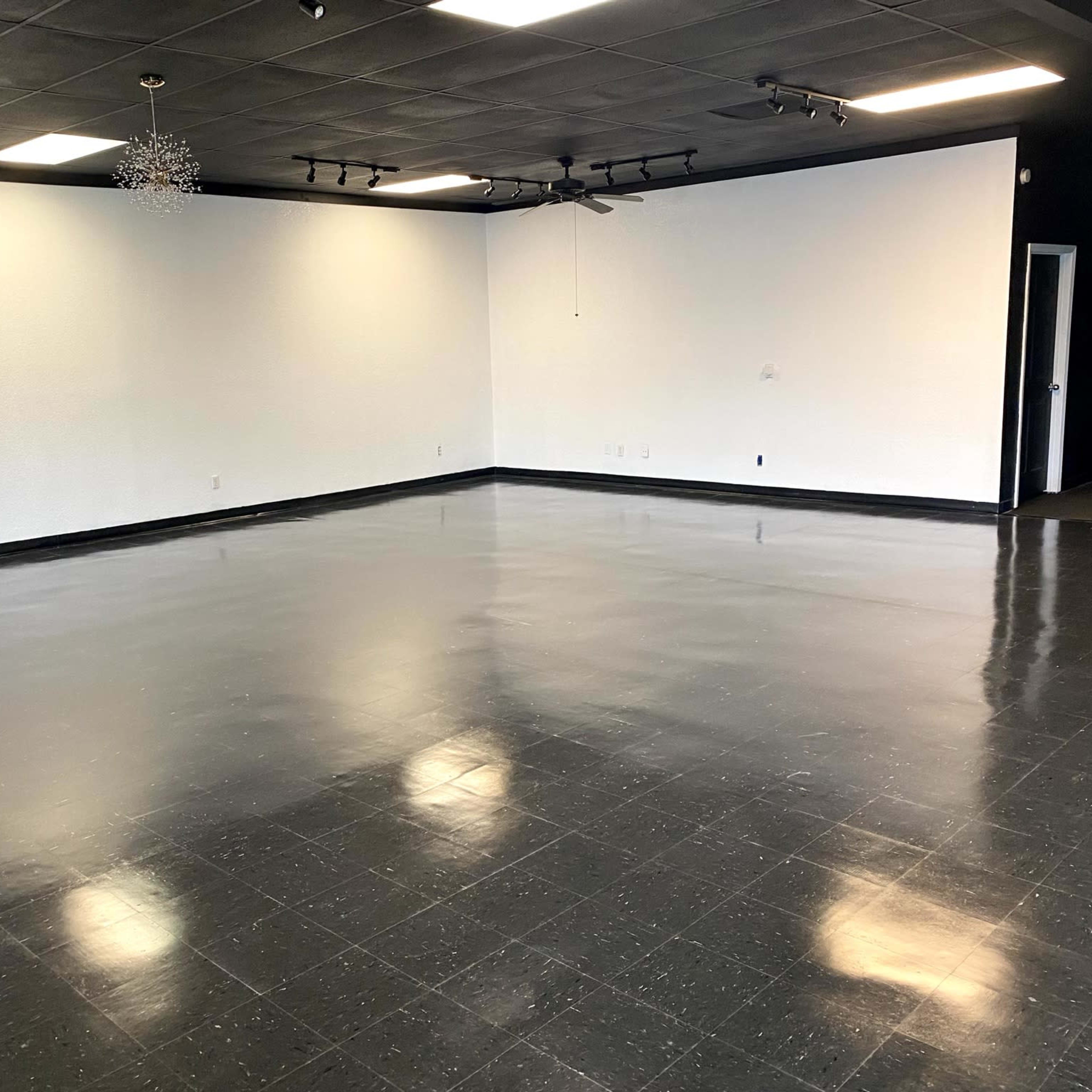A spacious, empty room with a shiny black floor and white walls, illuminated by ceiling lights.