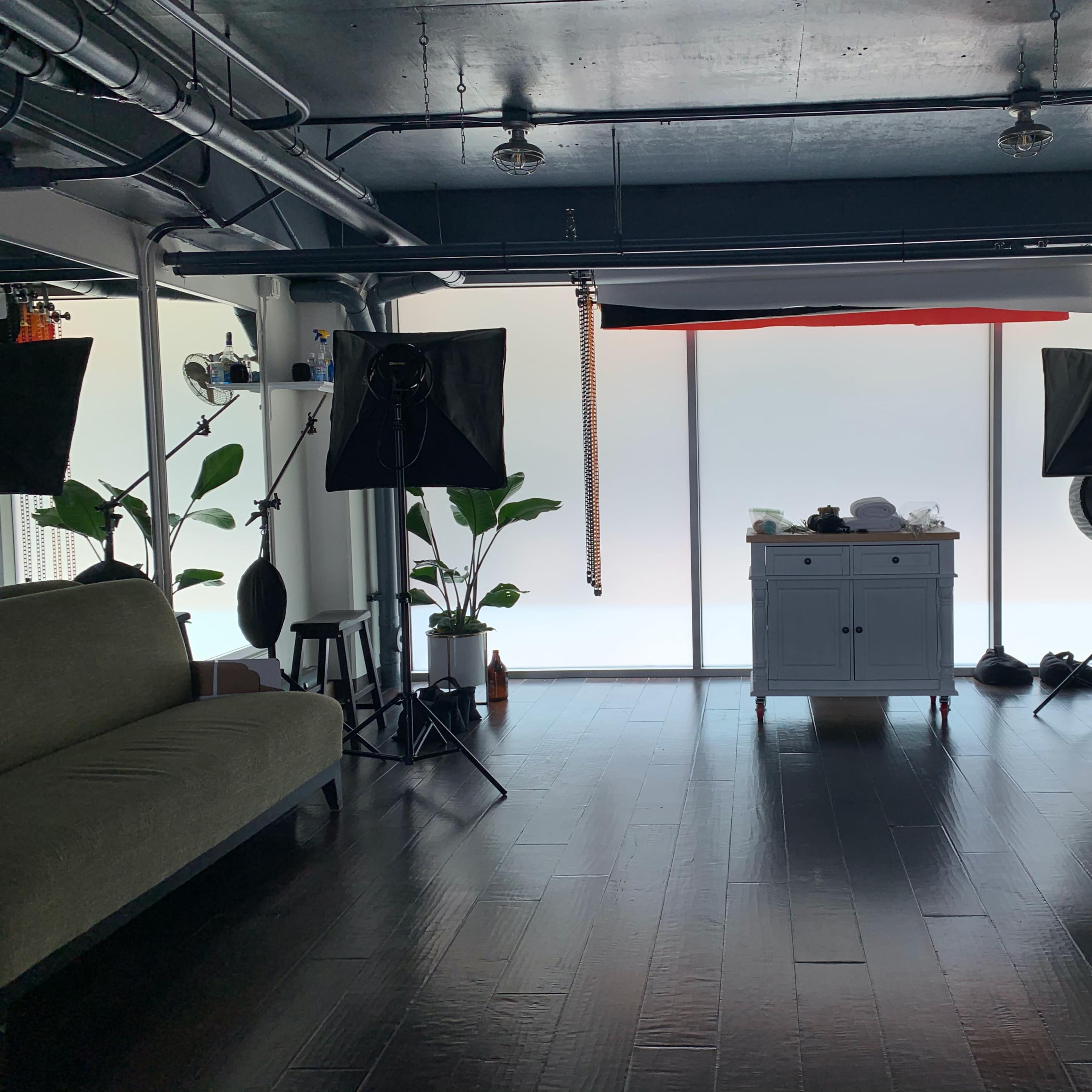 A spacious studio with a wooden floor, a sofa on one side, and photography equipment set up around a central white cabinet.