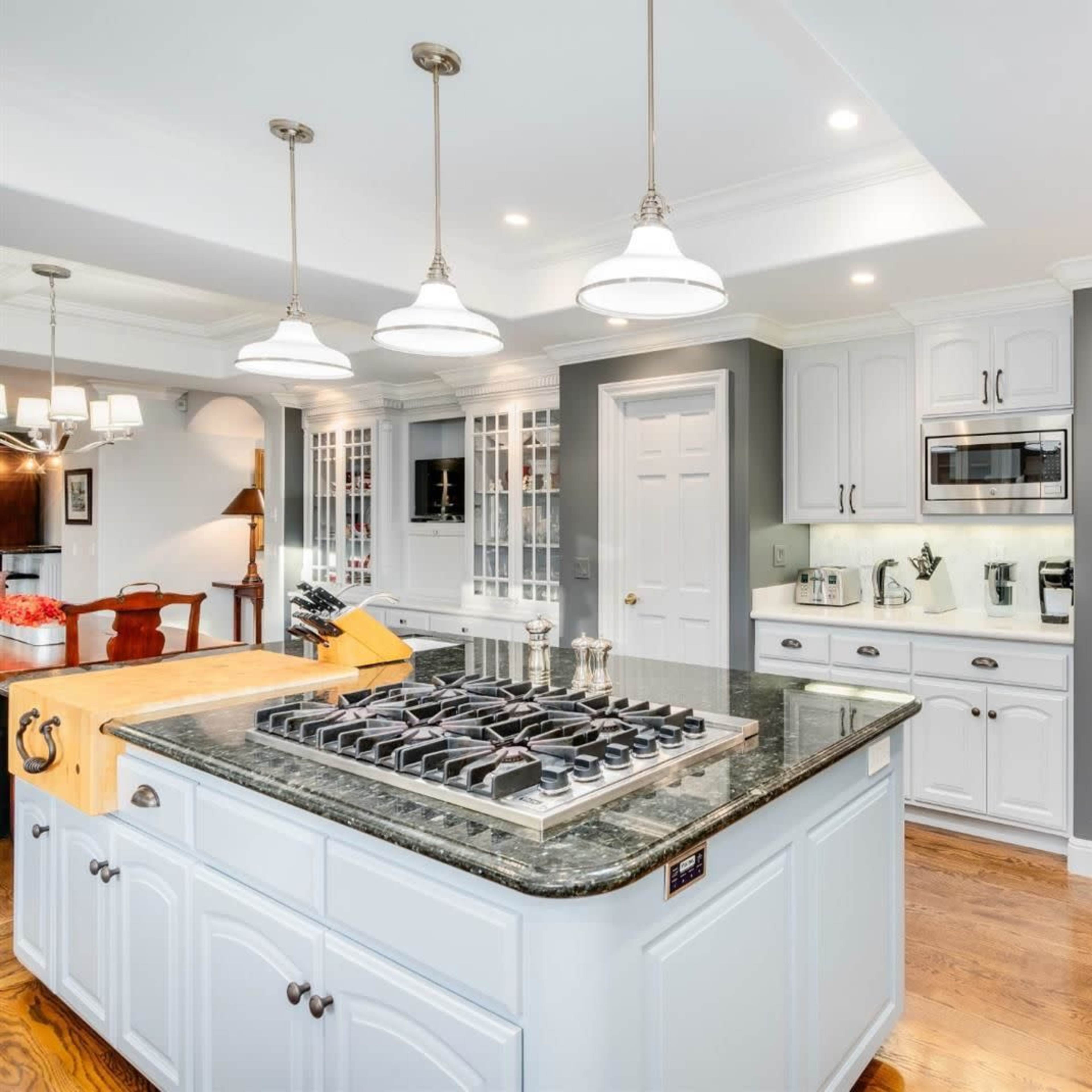 A spacious kitchen with a central island featuring a gas stovetop, white cabinetry, and an adjoining pantry area with a decorative wrought iron door.