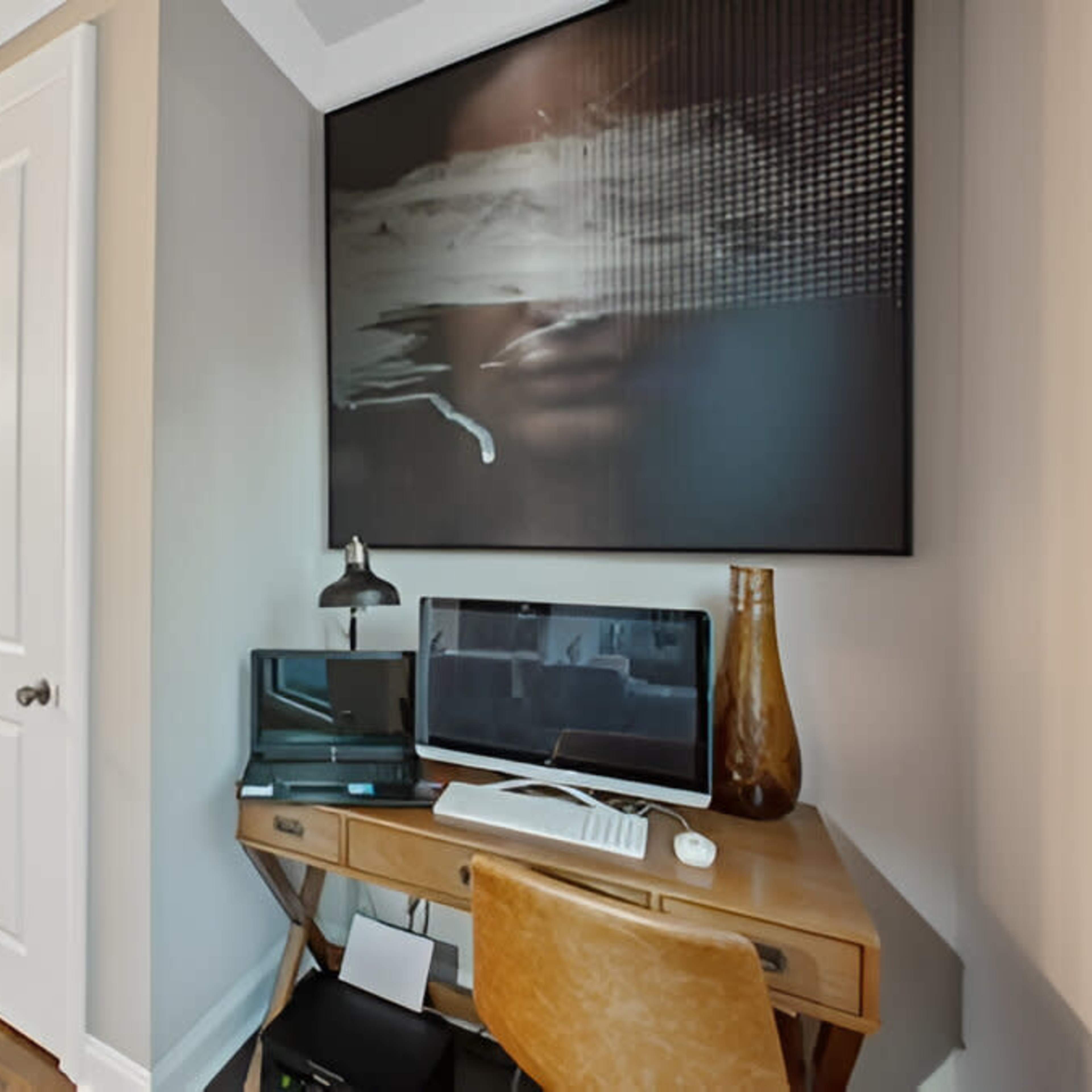 A small home office area features a desk with a computer and lamp, adjacent to a bathroom with a closed door.