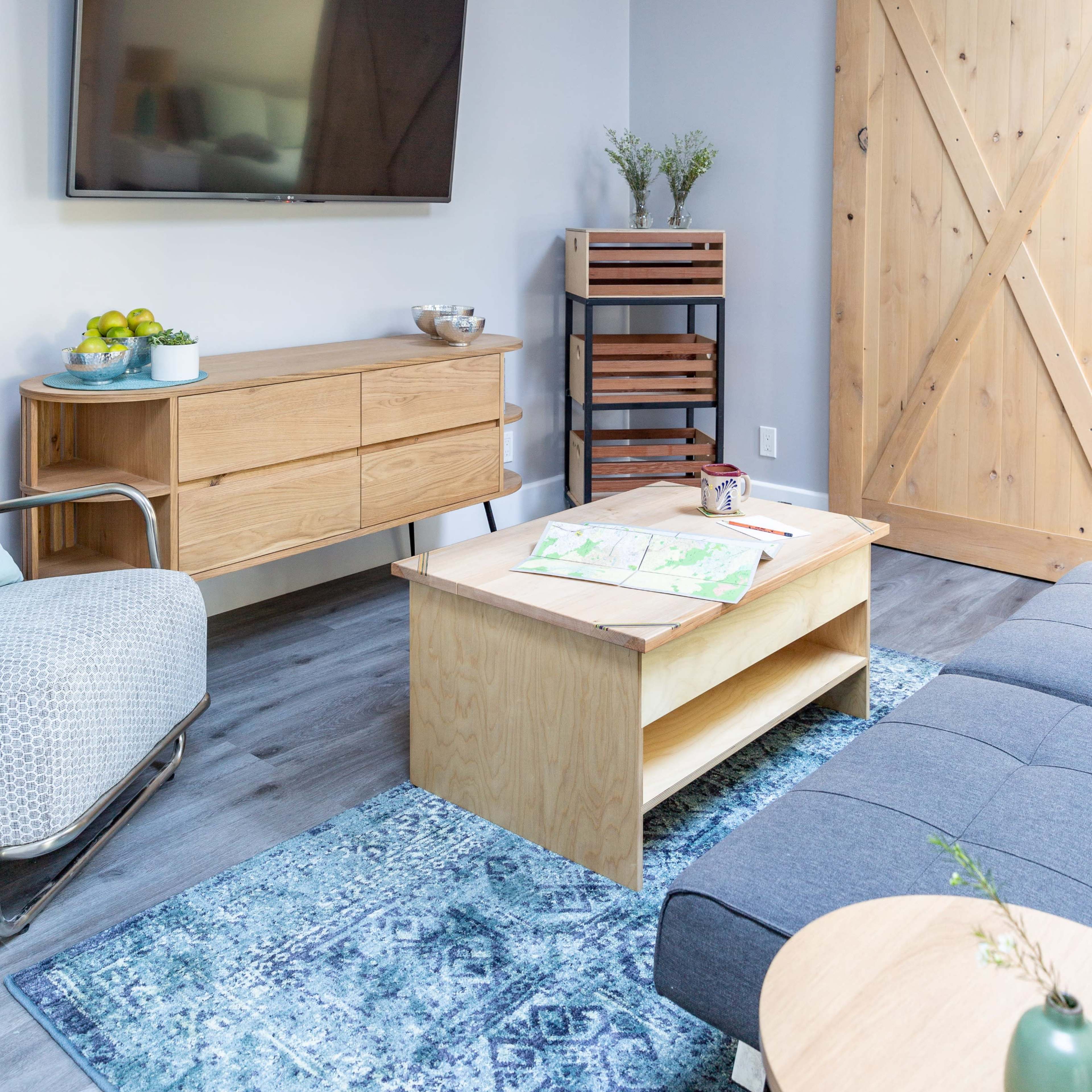 The living room features a flat-screen TV mounted on the wall, a wooden sideboard, a coffee table with a map, and a sliding barn door.