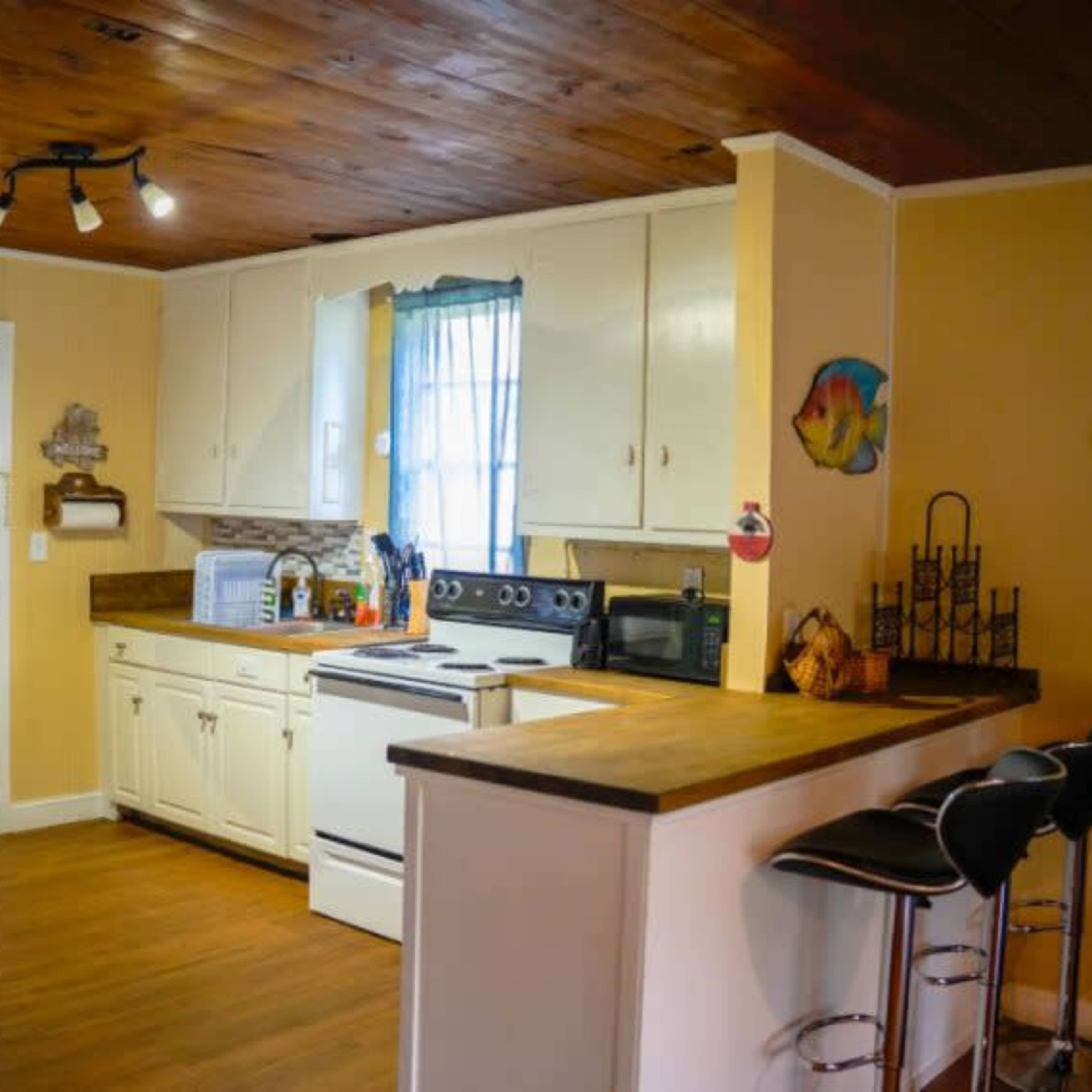 A kitchen with white cabinets, a wooden countertop, and a bar with three black stools.