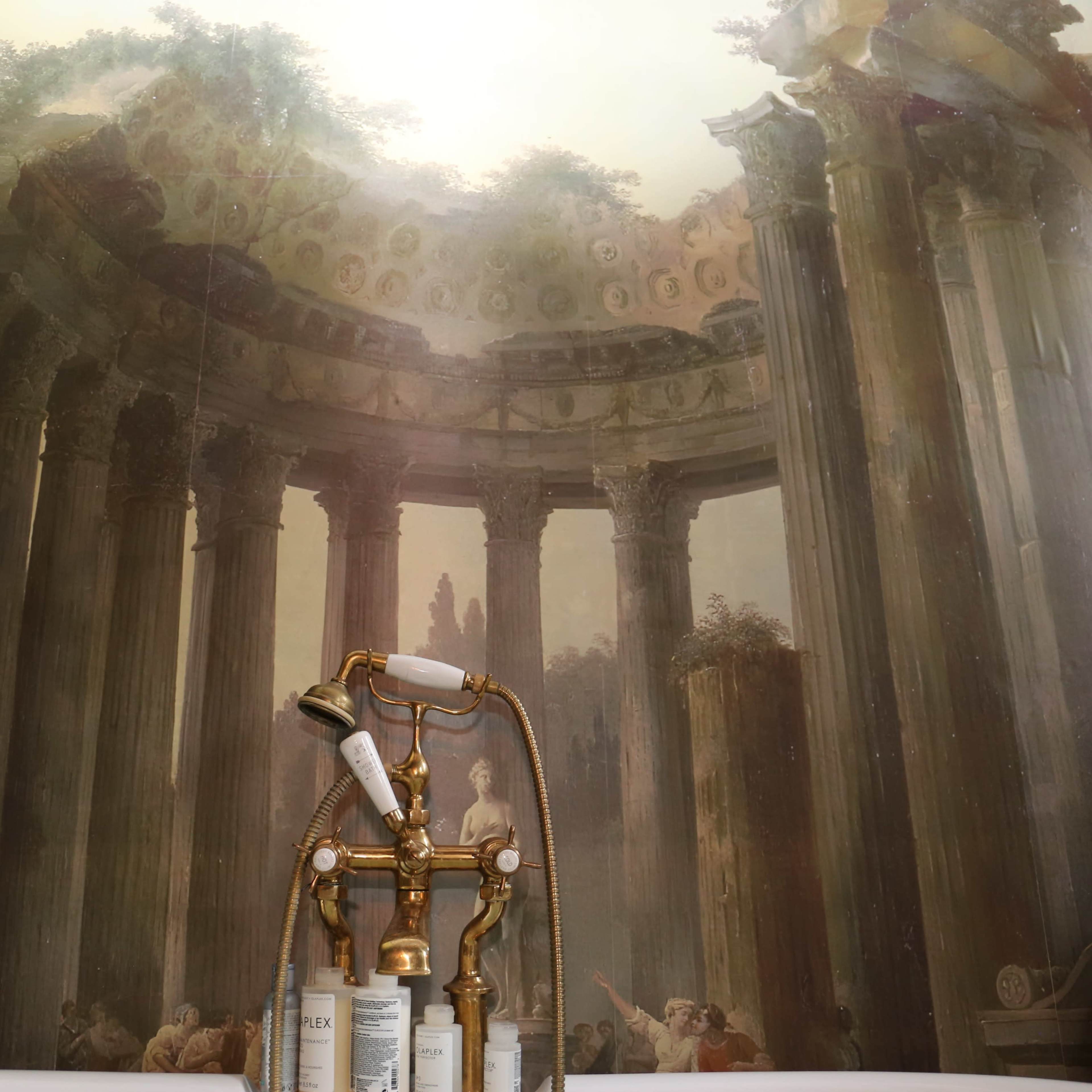 A bathroom with a mural depicting ancient columns and a classical scene, contrasted by vintage plumbing fixtures in the foreground.