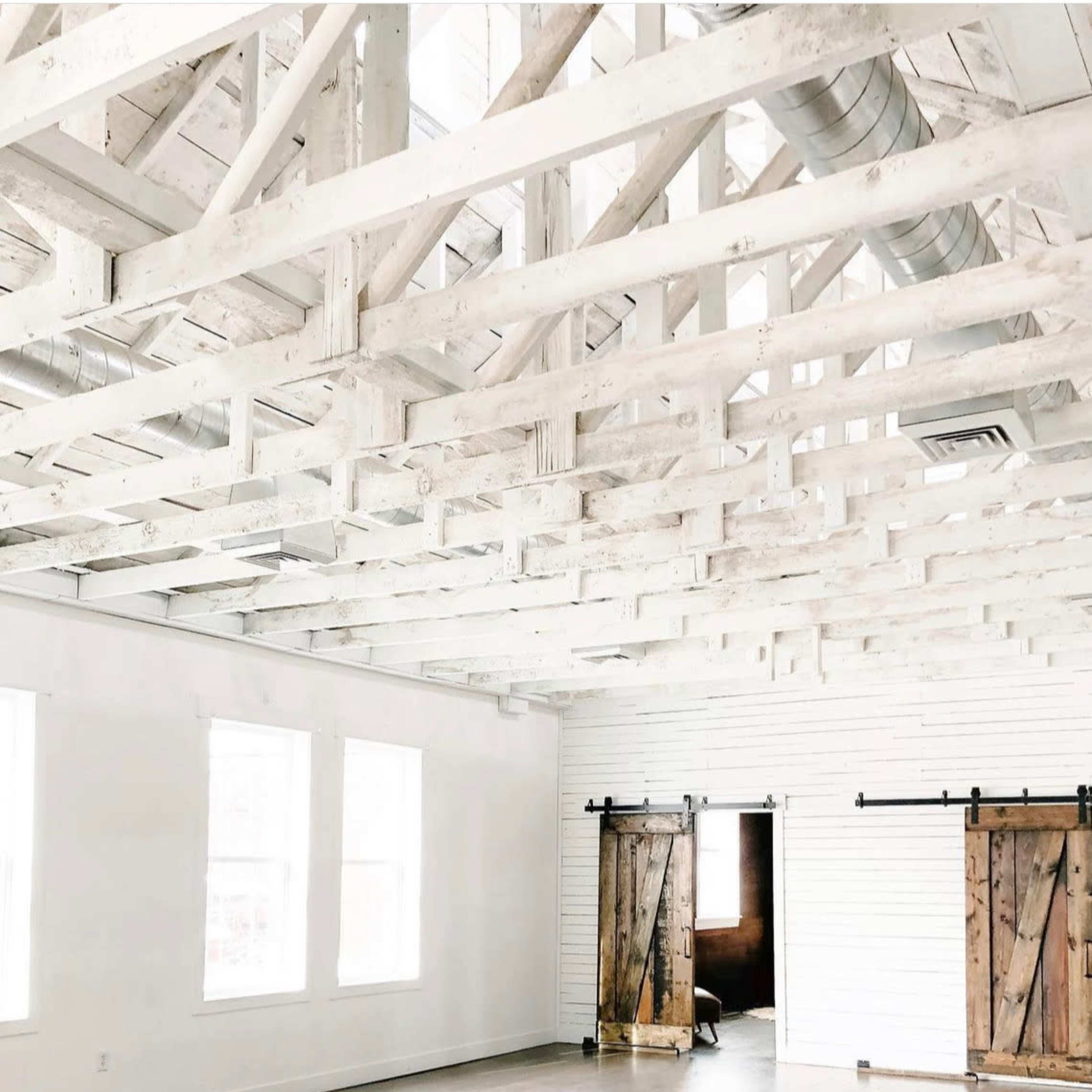 A spacious room with a white wooden ceiling and two large barn-style doors on opposite sides.