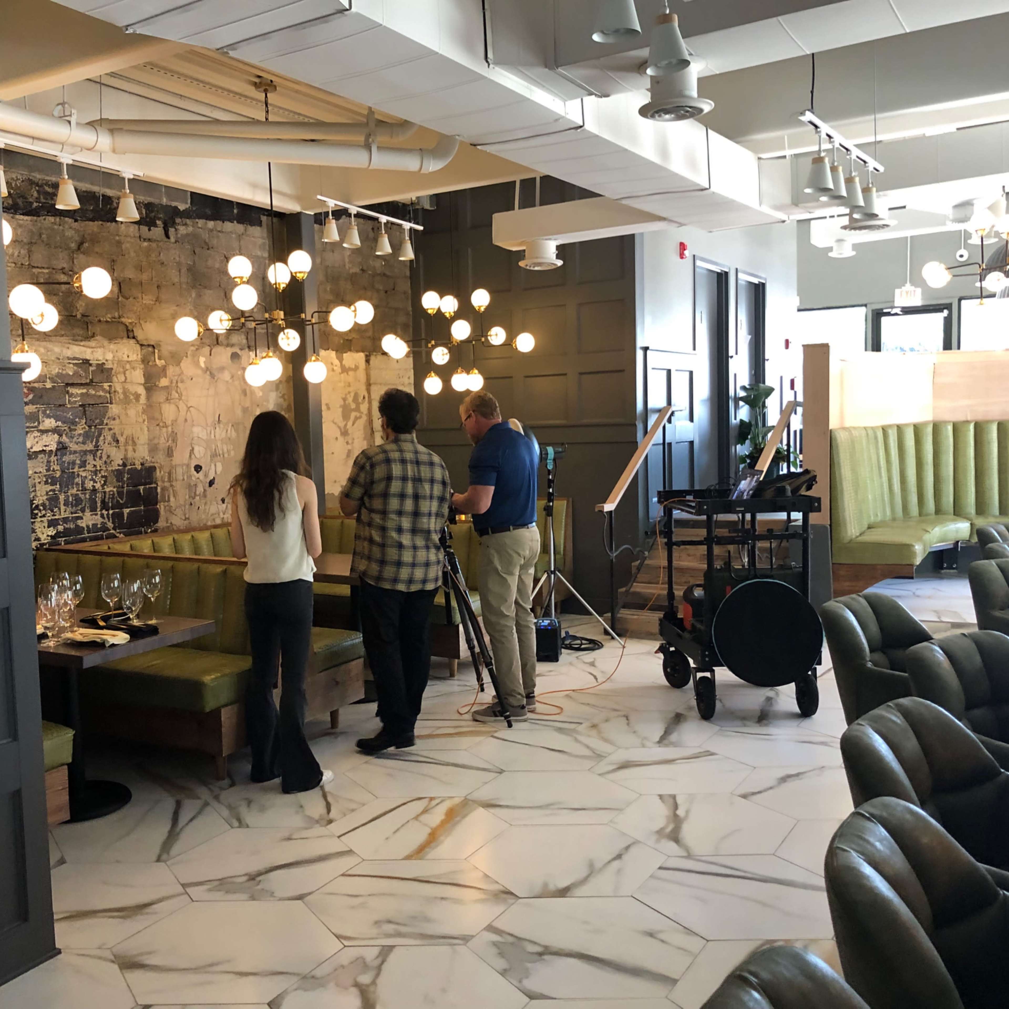 Three individuals are setting up filming equipment in a restaurant with modern decor and distinct lighting.