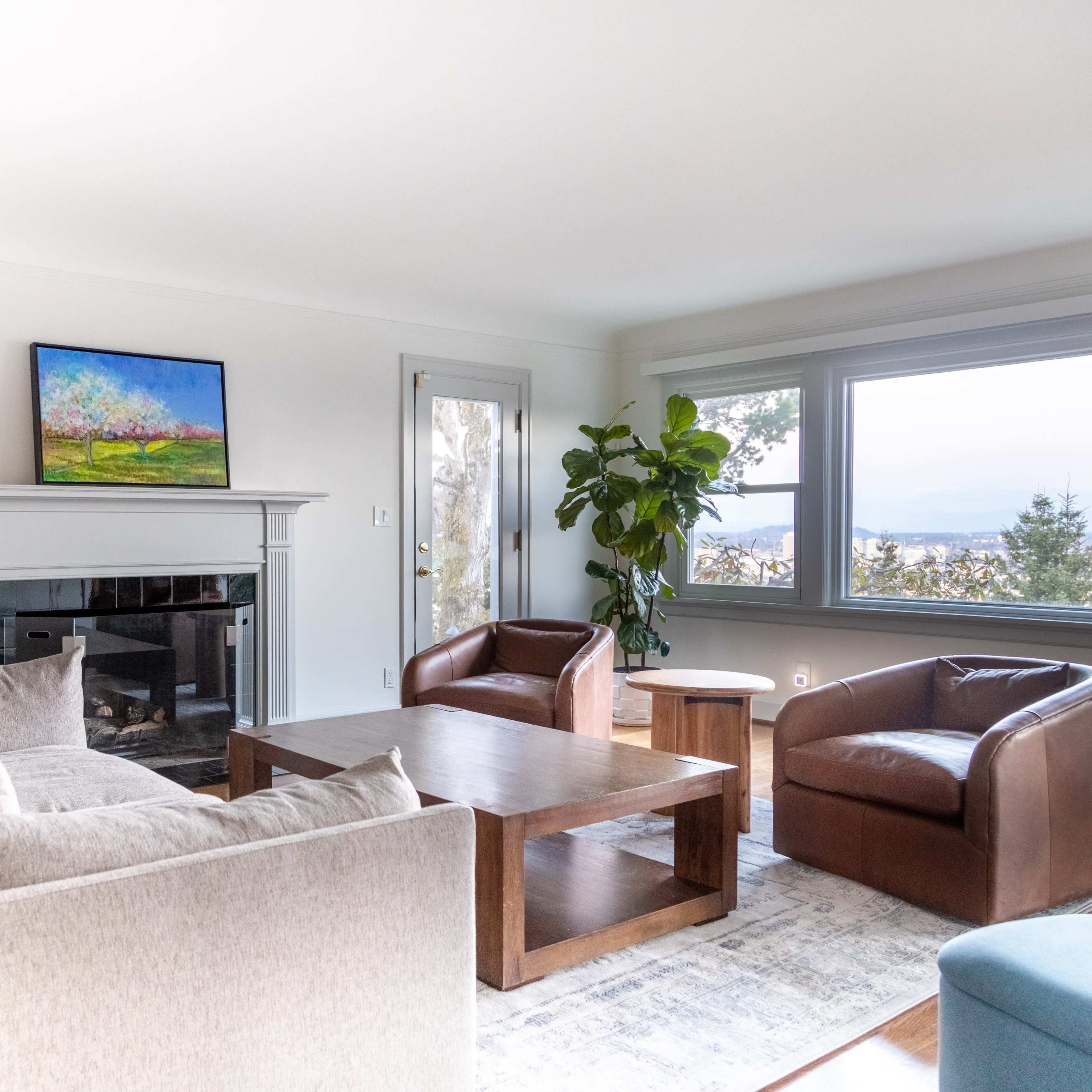 A modern living room featuring a beige sofa, two brown armchairs, a wooden coffee table, and a large window with a view.