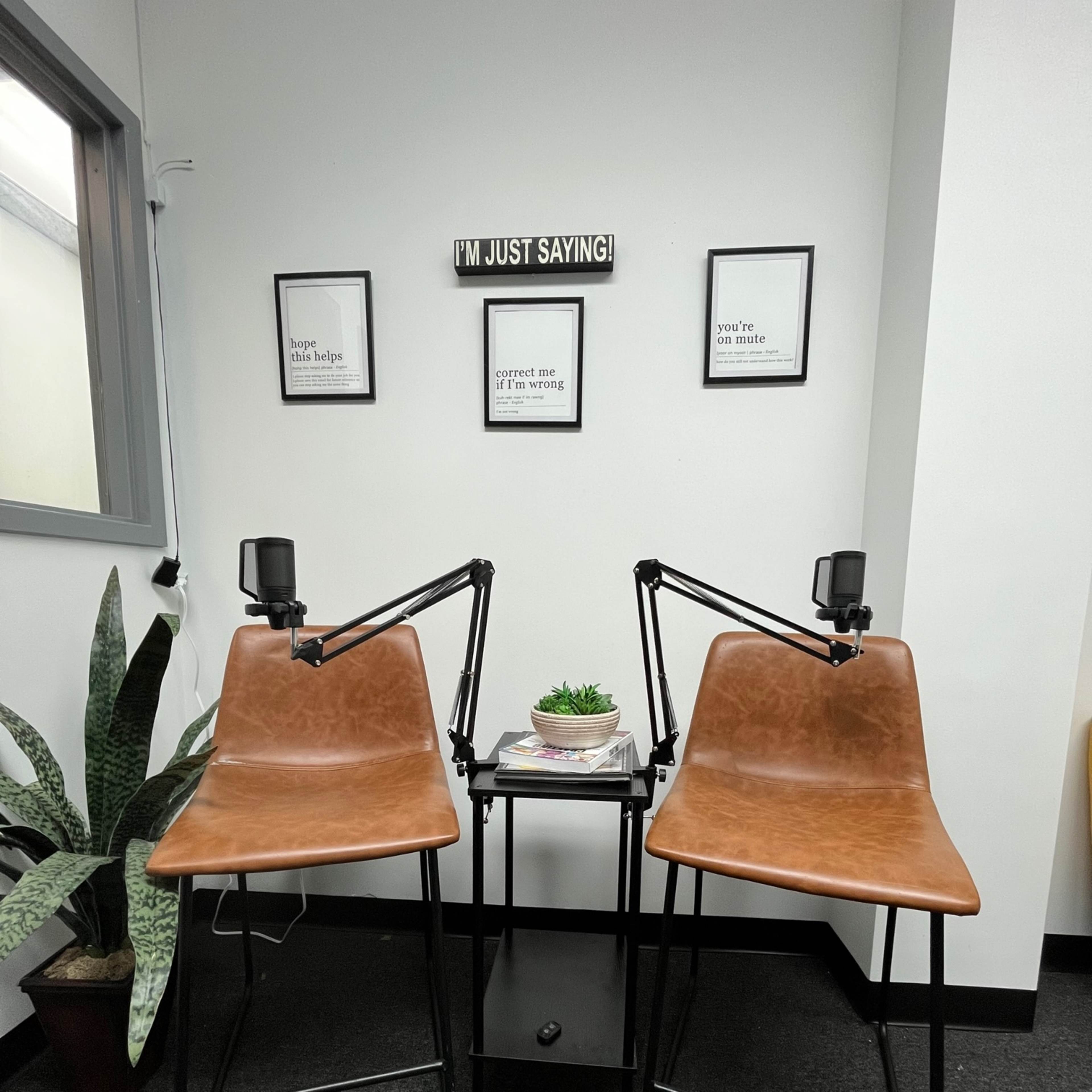 Two chairs are positioned at a small table with a plant in the center, set against a wall with motivational framed quotes.