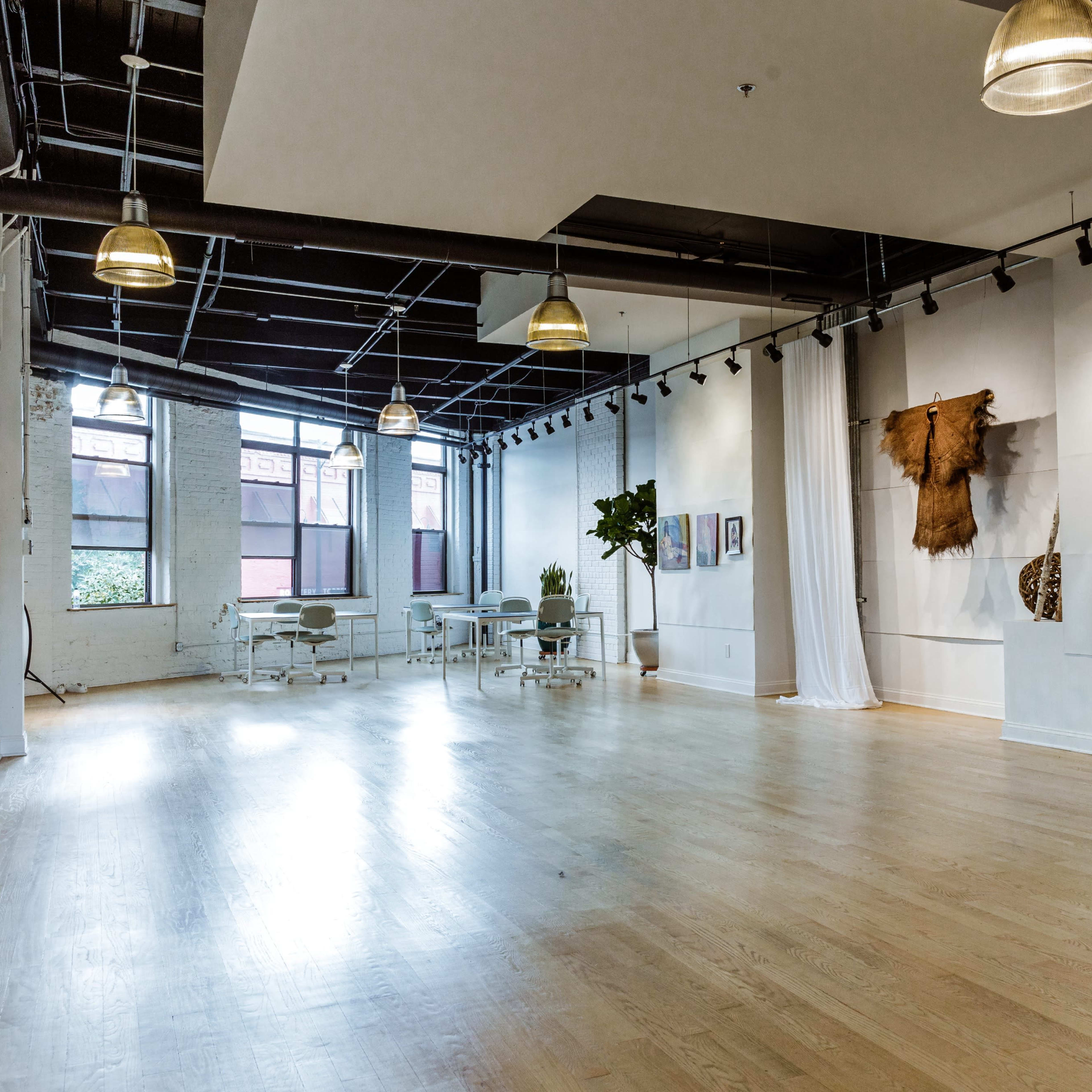 A spacious, well-lit interior with hardwood floors, featuring modern lighting fixtures and a few pieces of artwork on the walls.