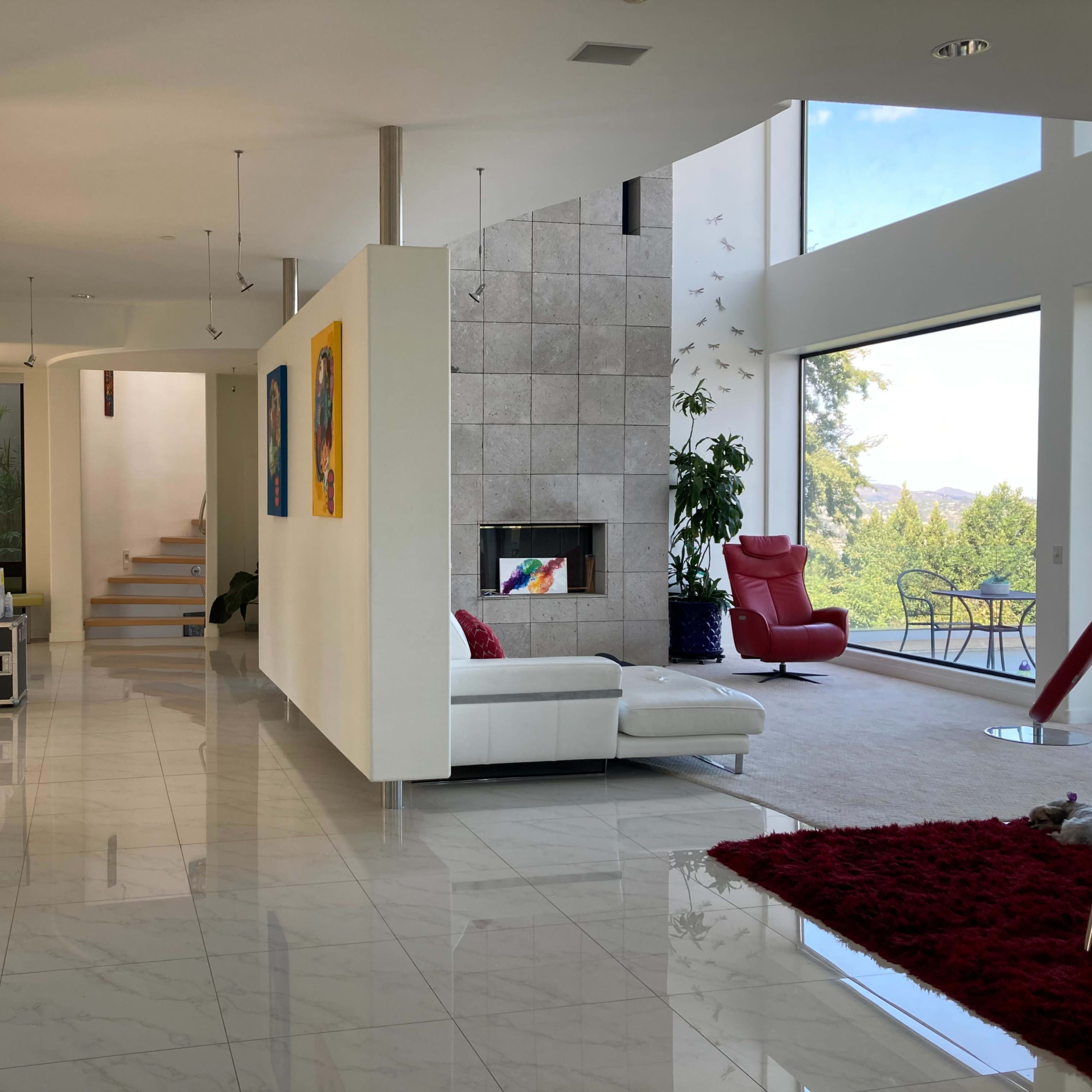 A modern interior space featuring a bright living area with a white sectional sofa, large windows, and a staircase leading to an upper level.