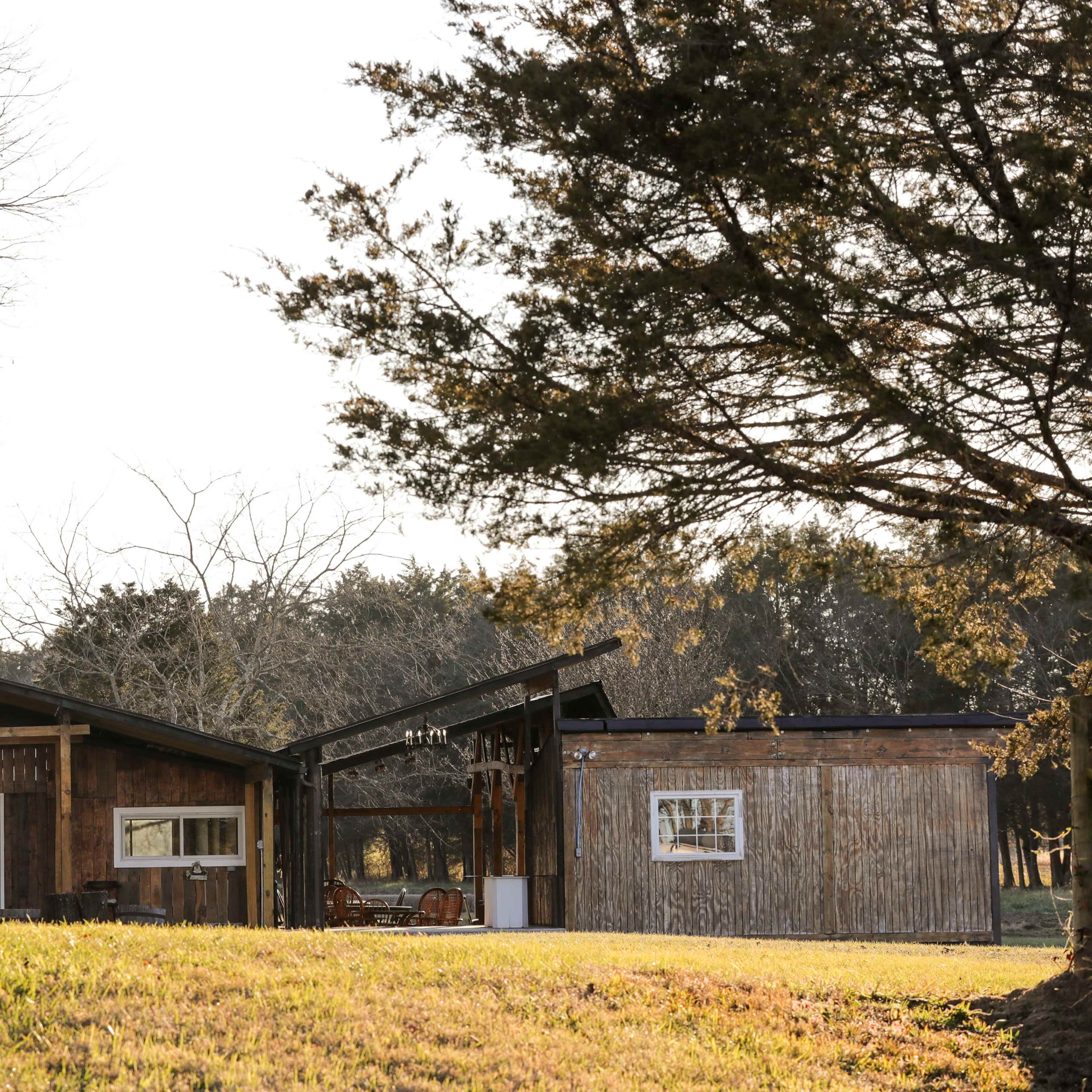 A rustic wooden cabin with a large porch sits in a grassy area surrounded by trees.