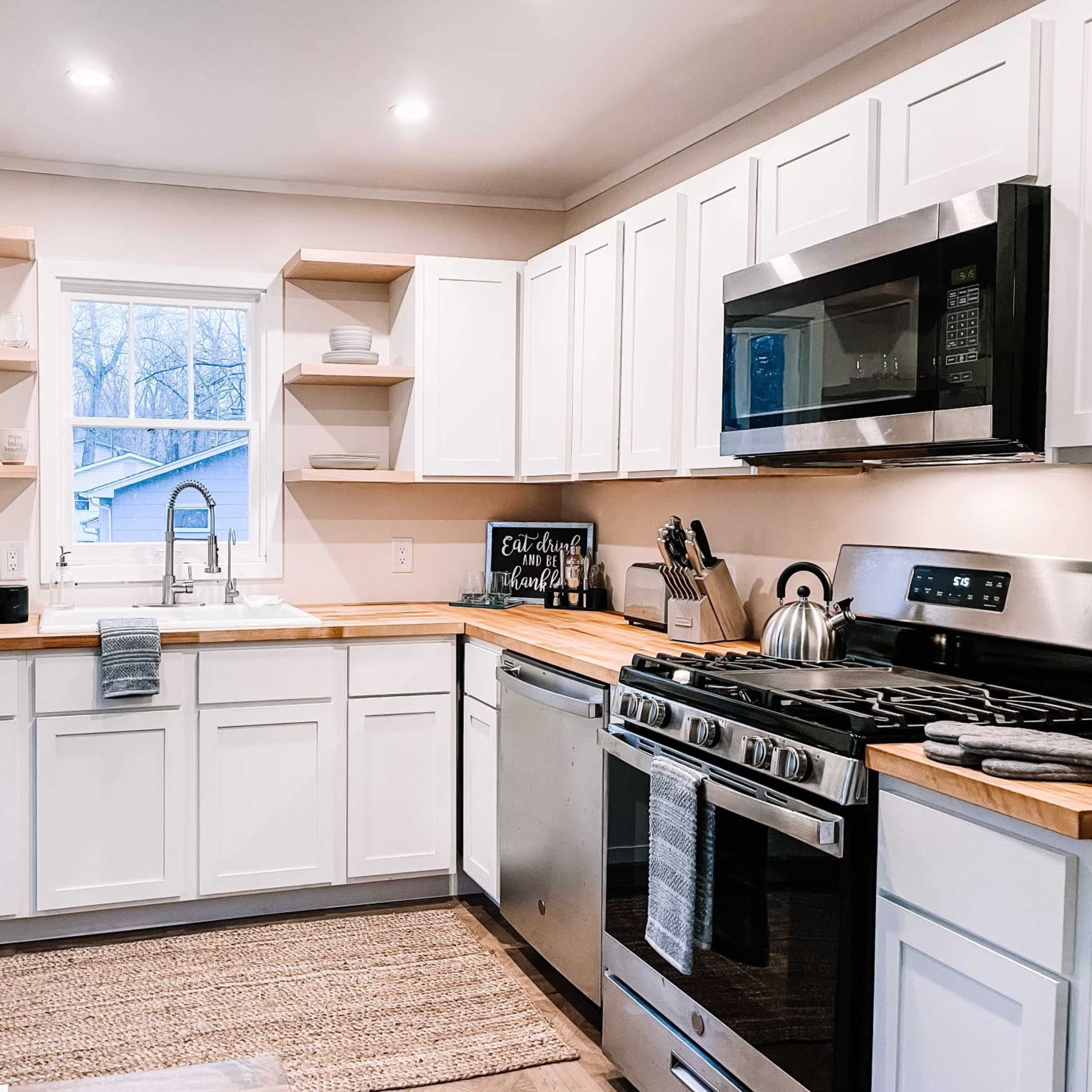A modern kitchen features white cabinets, stainless steel appliances, and a wooden countertop with a window above the sink.