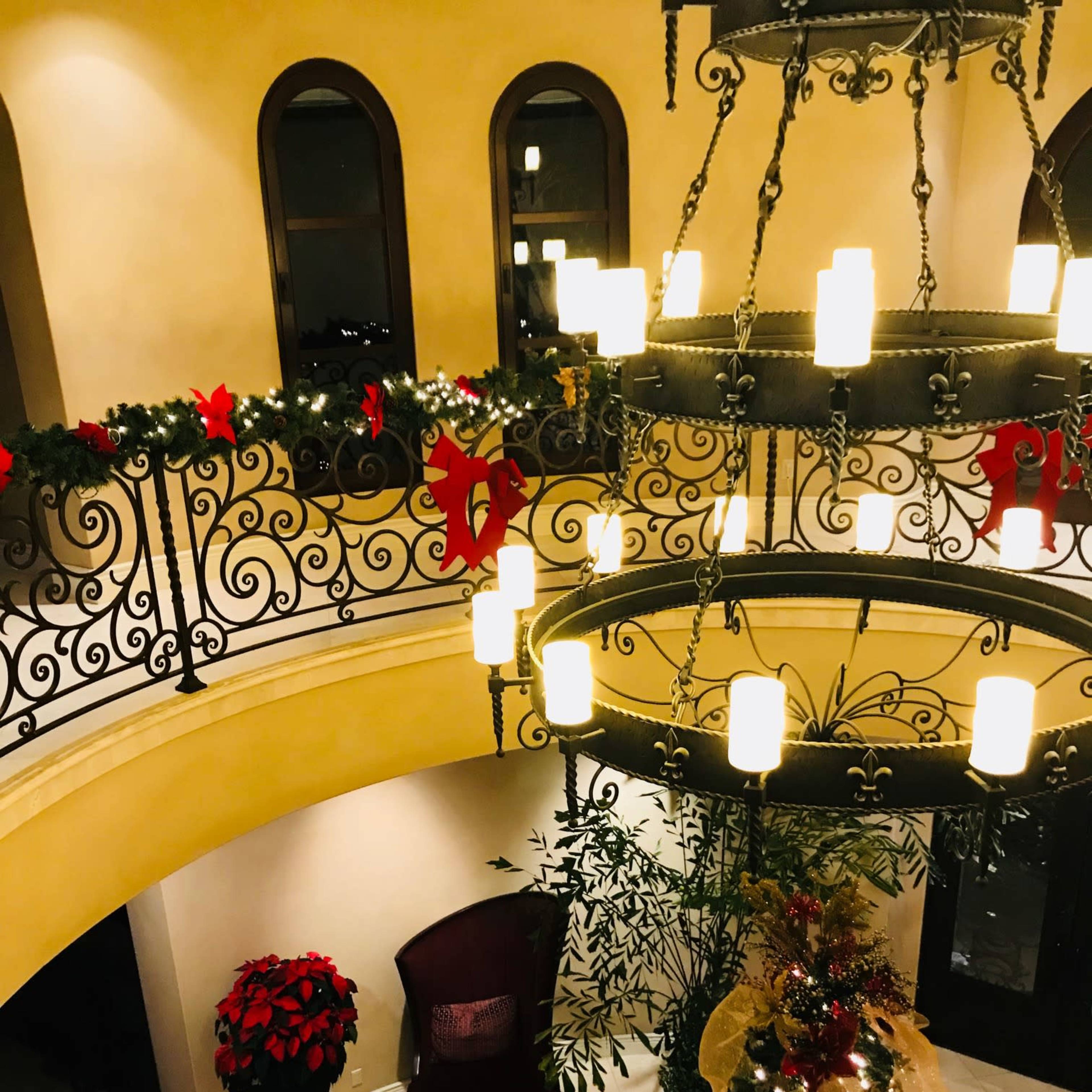 A well-decorated entryway with a large chandelier, a Christmas tree, and festive garlands adorning the balcony railing.