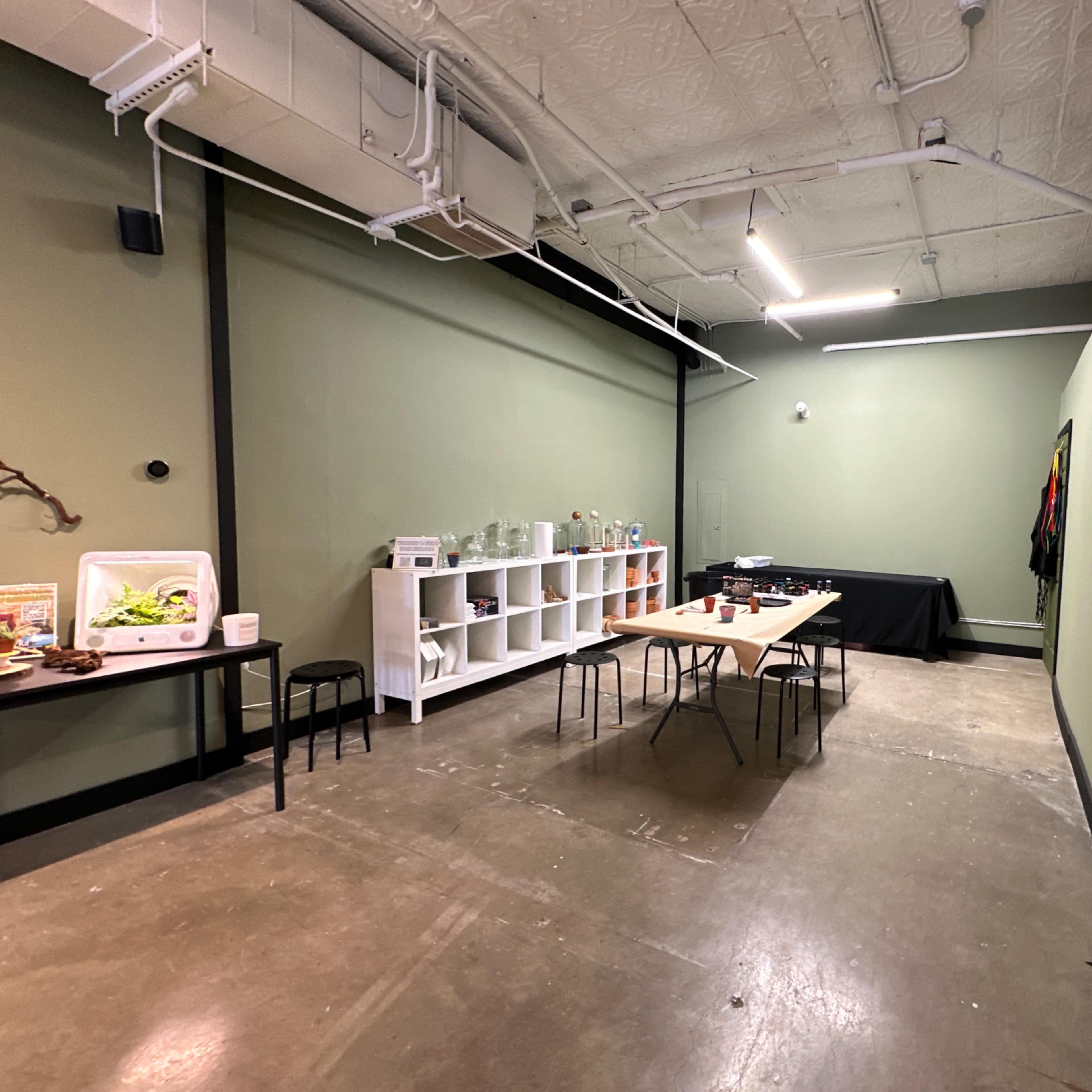 A sparse room with green walls, a polished concrete floor, and several tables set up along with shelving and a cooler.