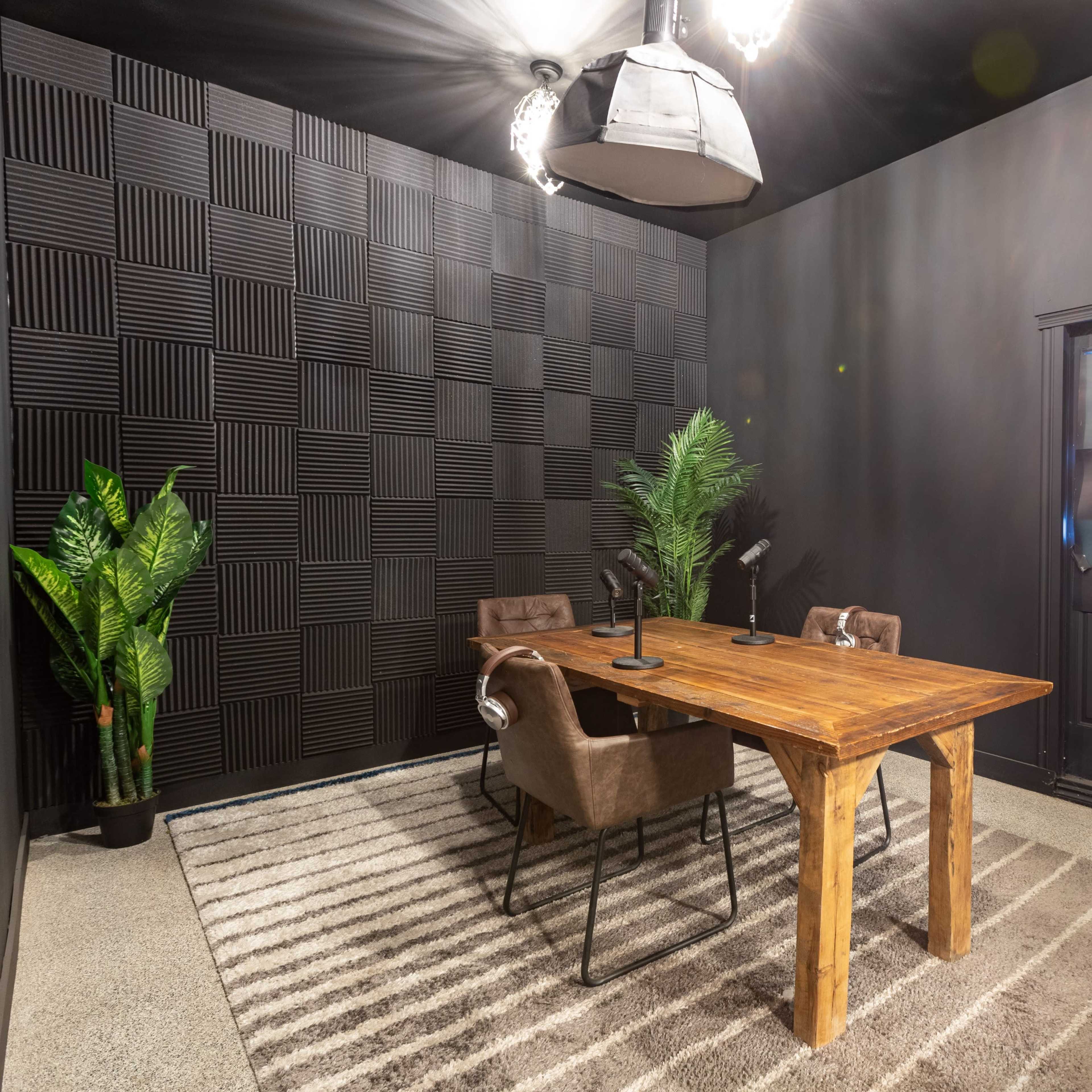 A small conference room with a wooden table, two chairs, a patterned rug, a potted plant, and a black door.