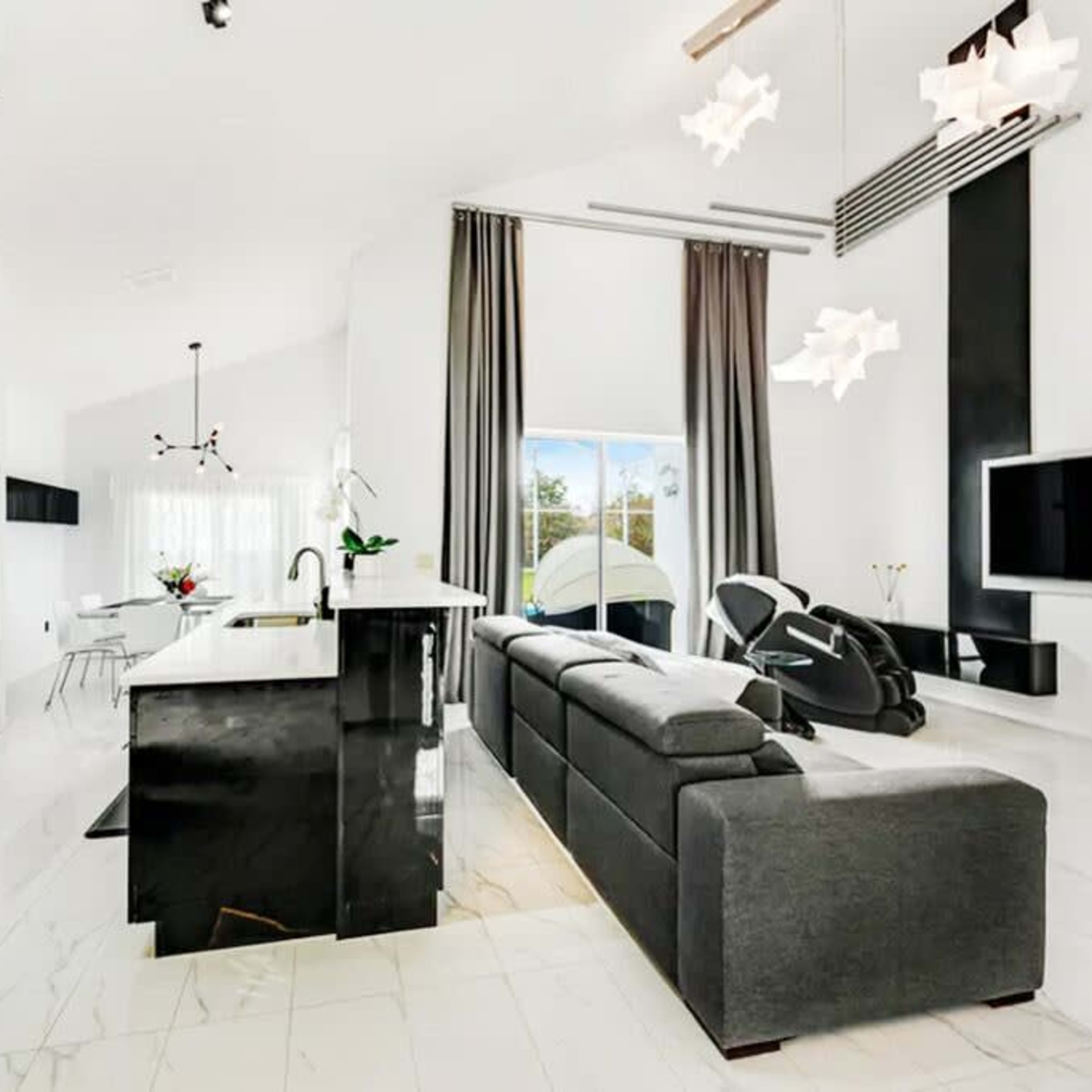 A modern open-plan kitchen and living area featuring sleek black cabinetry, a large gray sofa, and ample natural light from a window.