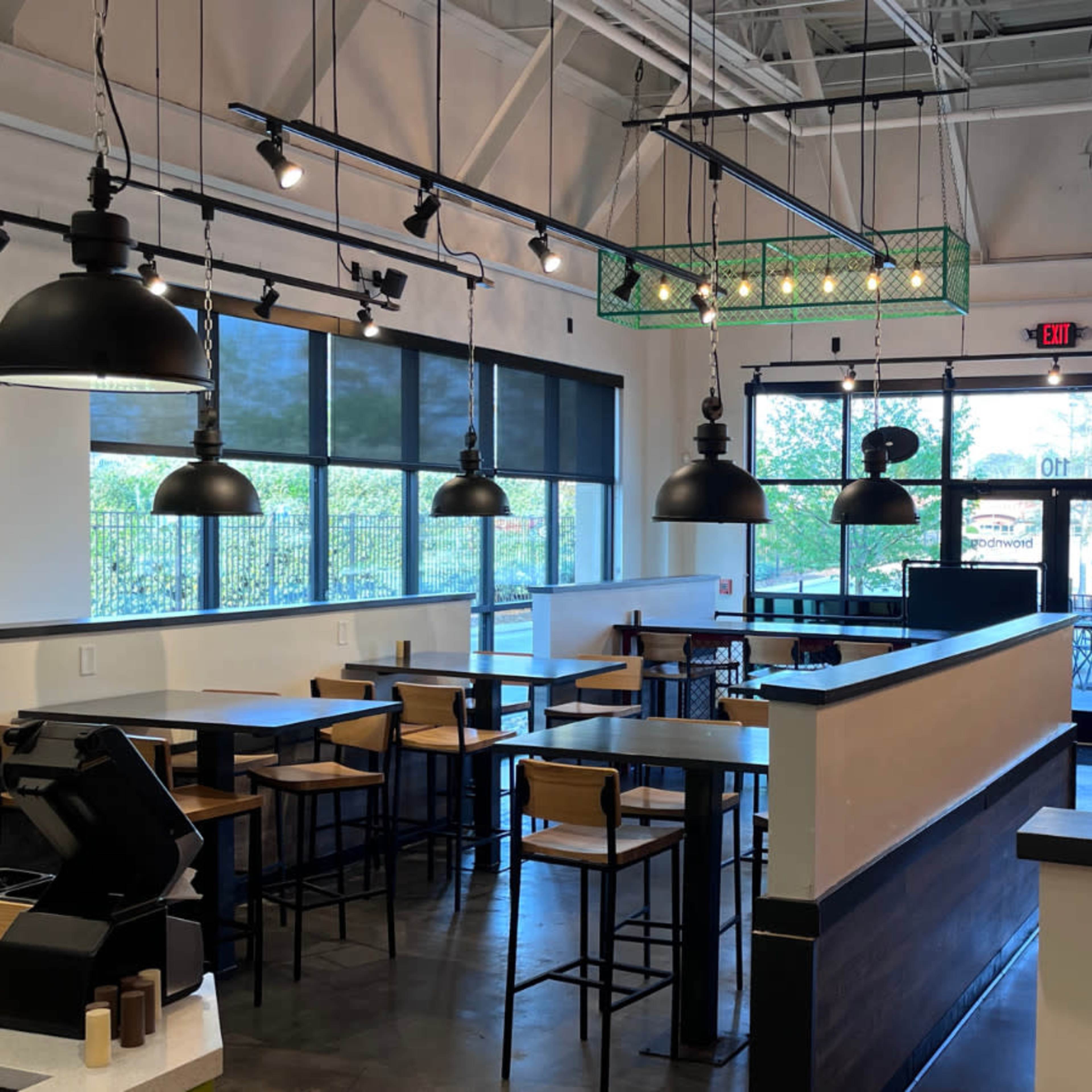 A modern cafe interior with black pendant lights, wooden tables and chairs, and large windows allowing natural light to enter.
