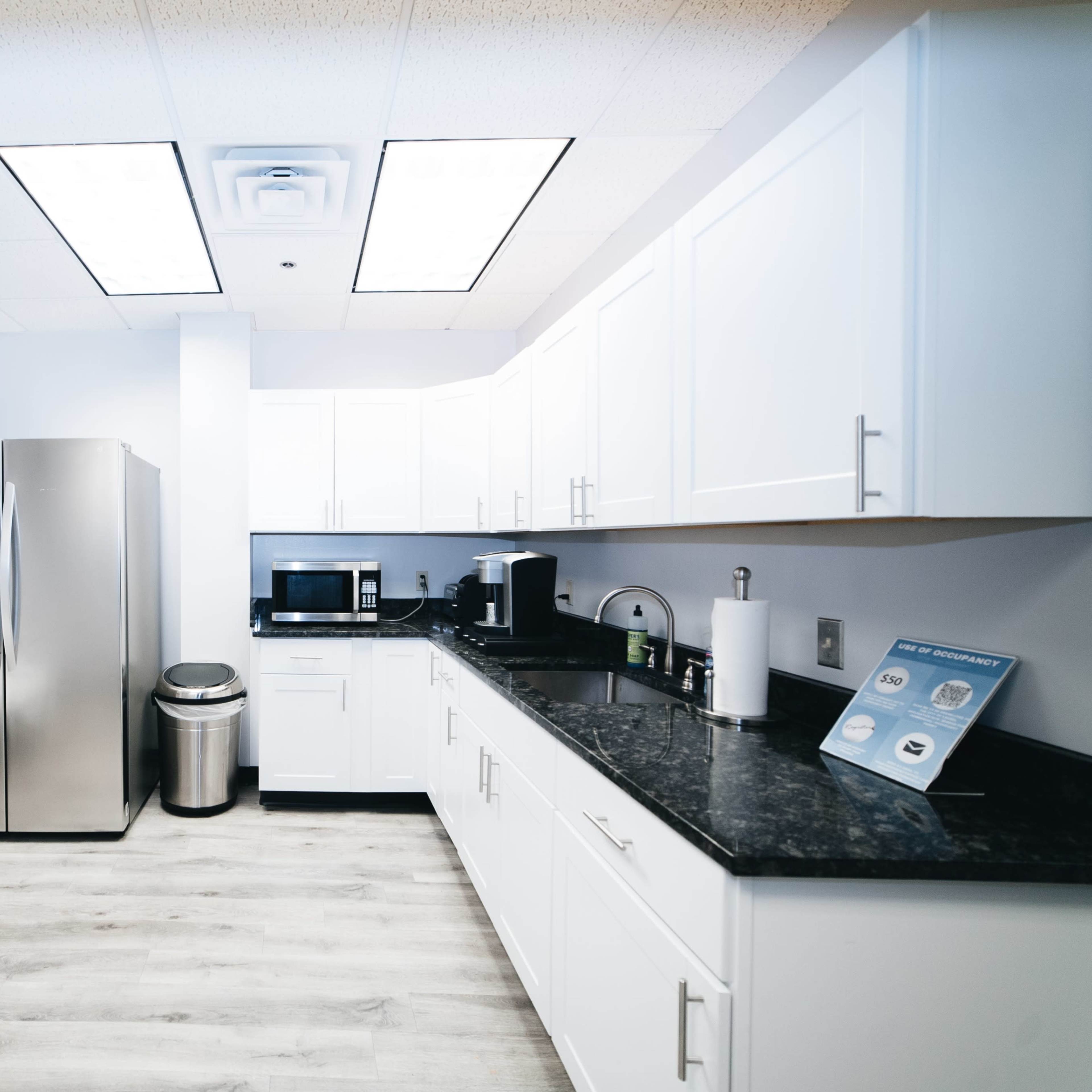 A modern kitchen with stainless steel appliances, a black countertop, and white cabinets.
