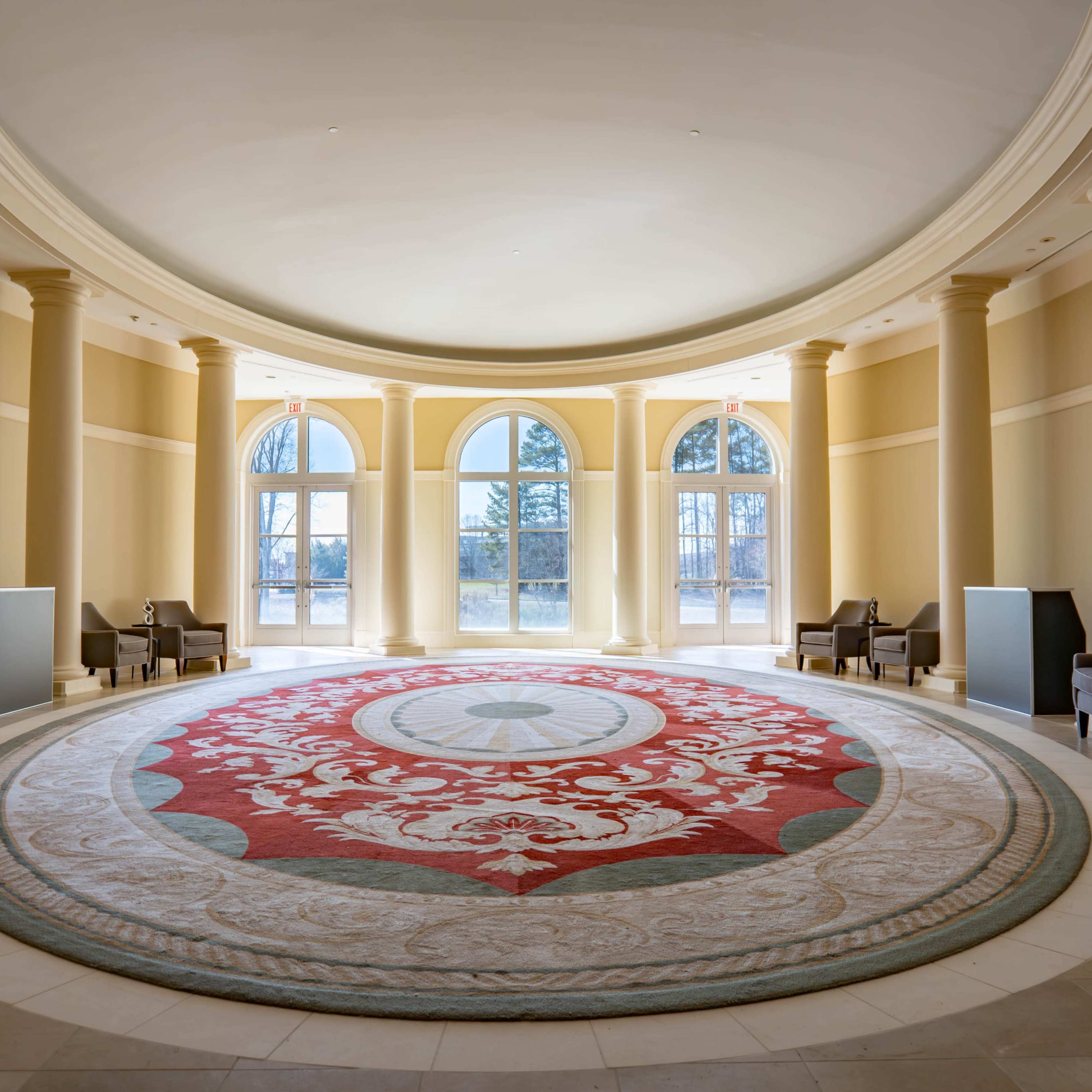 A circular room with a large, decorative rug at the center, surrounded by four tall windows and several seating areas.