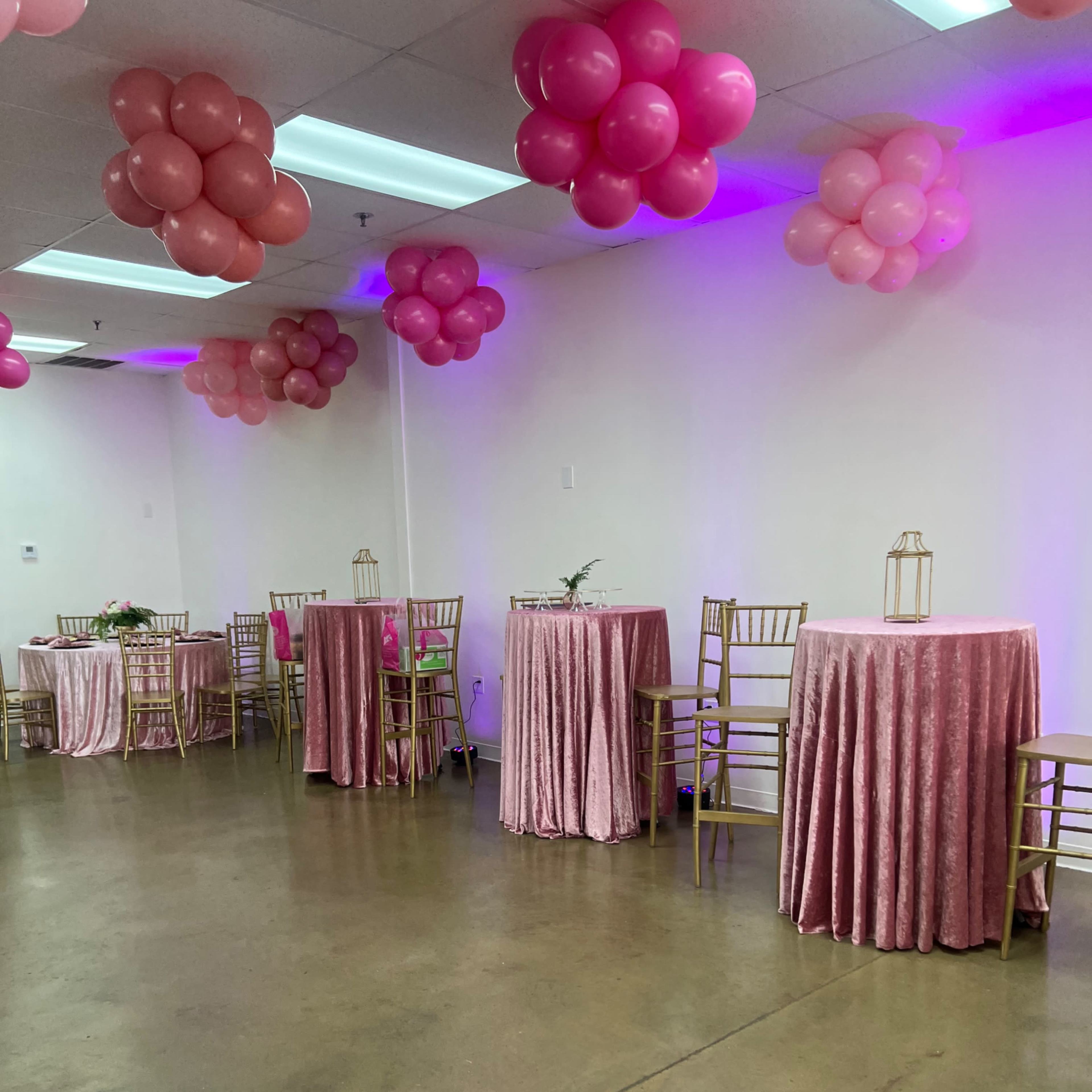 A room decorated with pink balloons and tables covered in pink tablecloths, set up for an event.