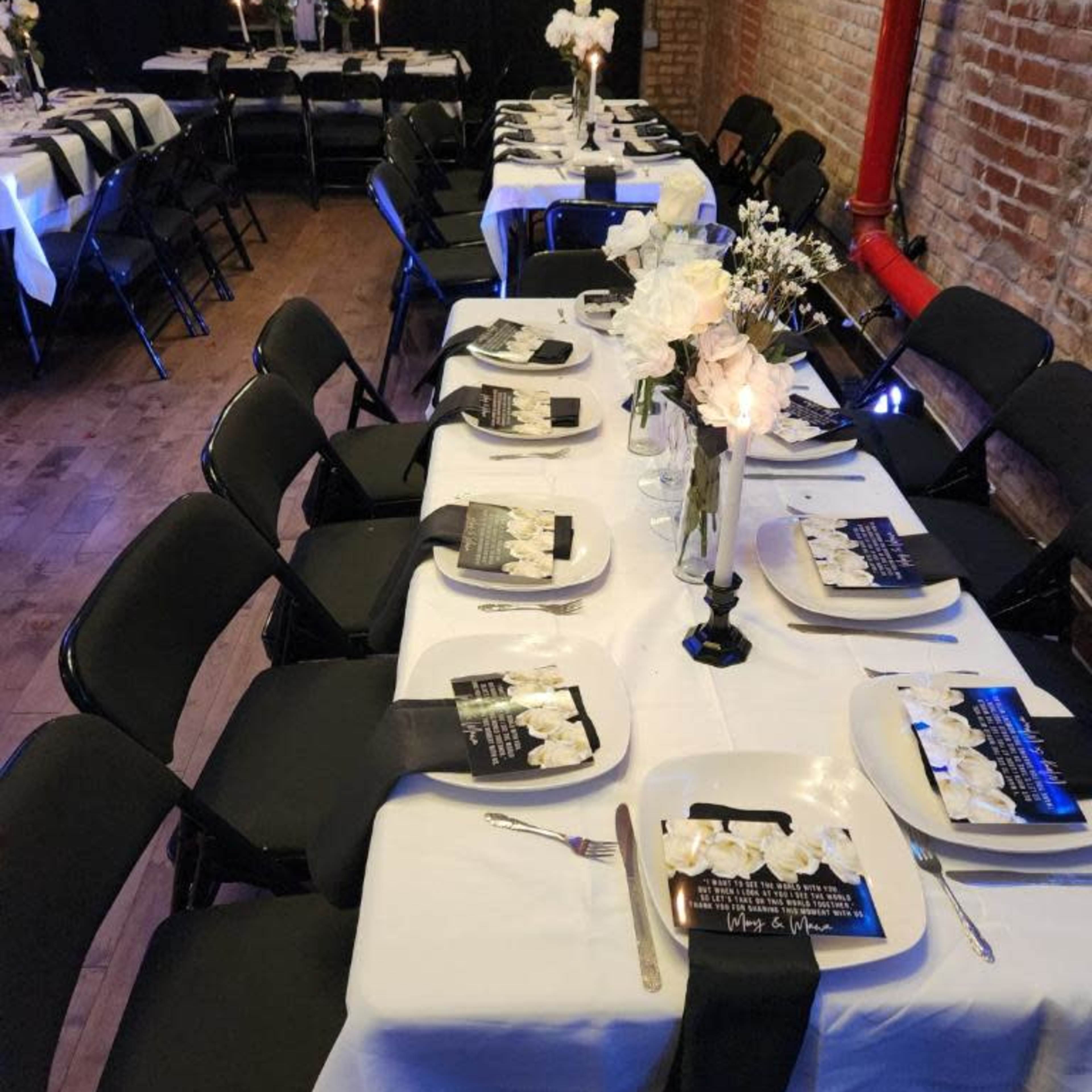 A decorated dining area with several tables covered in white tablecloths, black napkins, and floral centerpieces, arranged for an elegant event.
