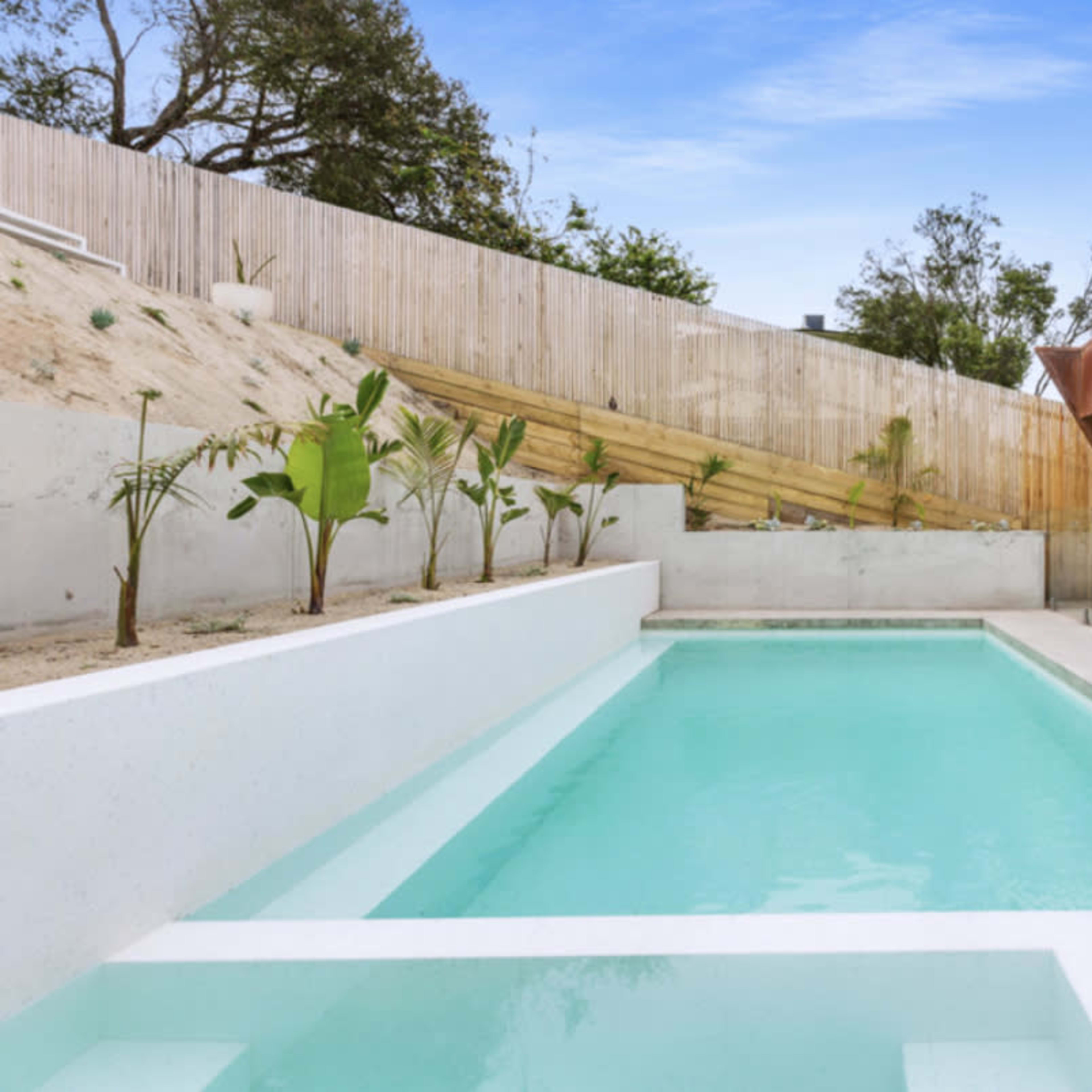 A rectangular swimming pool surrounded by minimalist landscaping and a modern house with large glass doors.