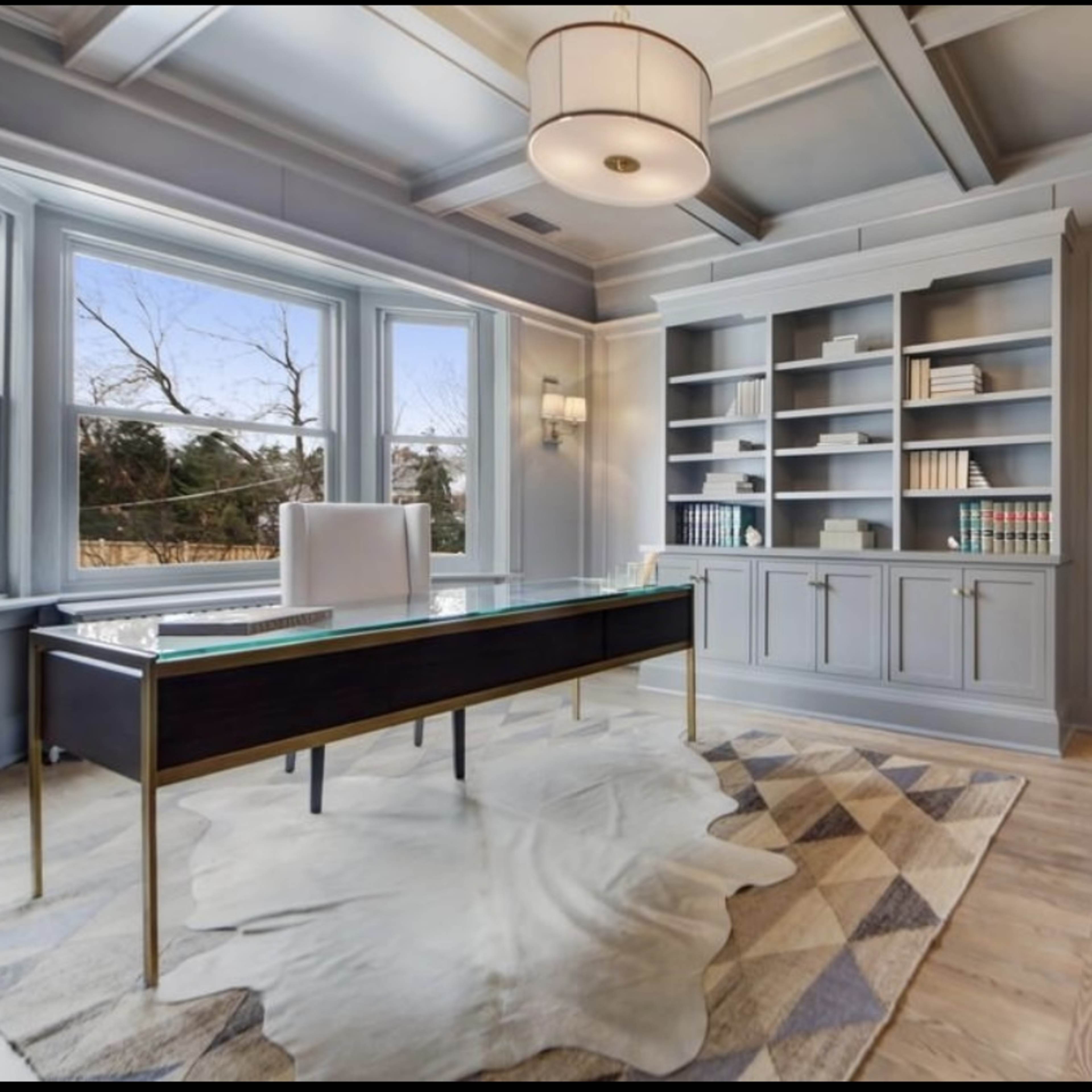 A well-designed office with large windows, a modern desk, a bookshelf filled with books, and a fireplace.