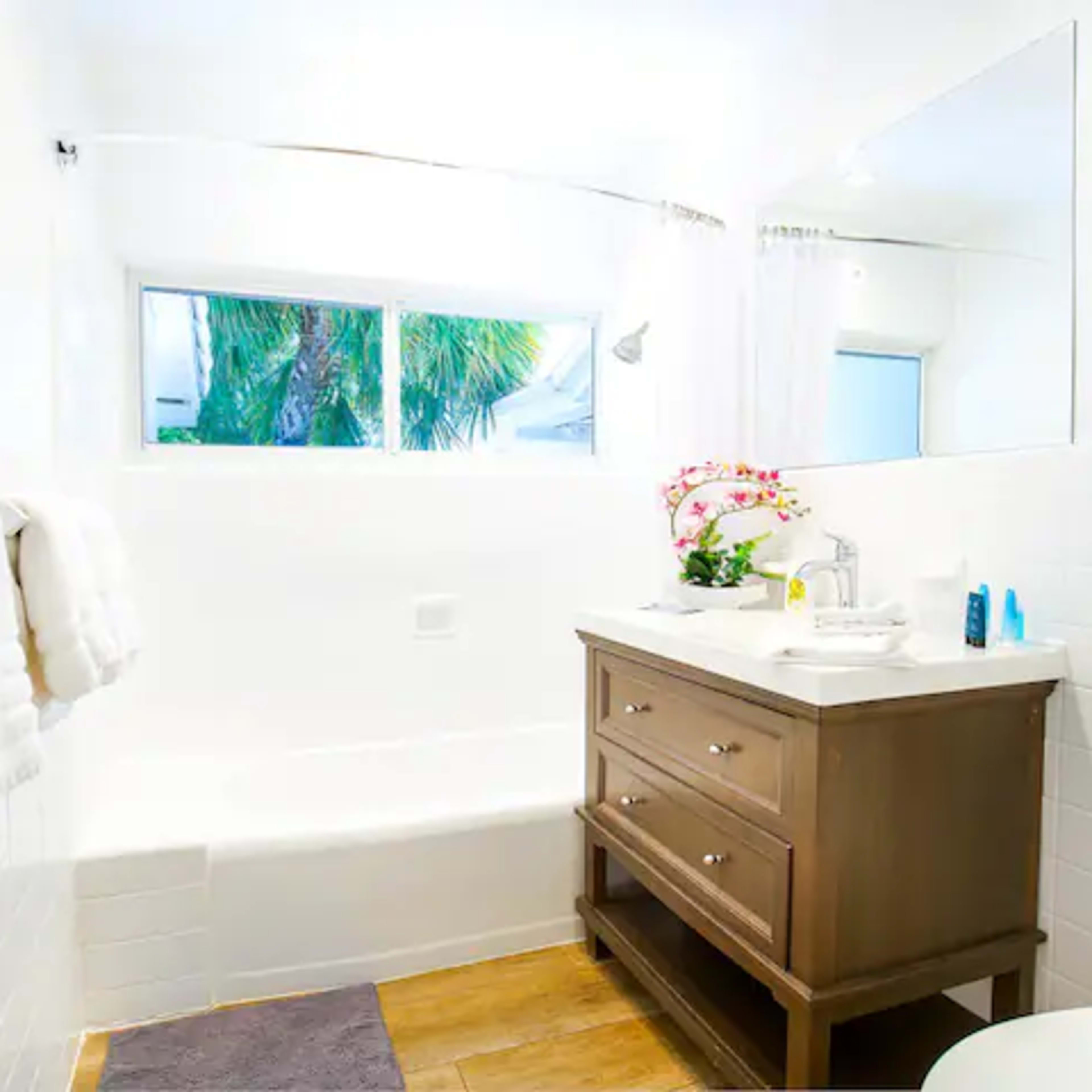 A bright bathroom features a white bathtub, a wooden vanity with a sink, and a window allowing natural light to enter.