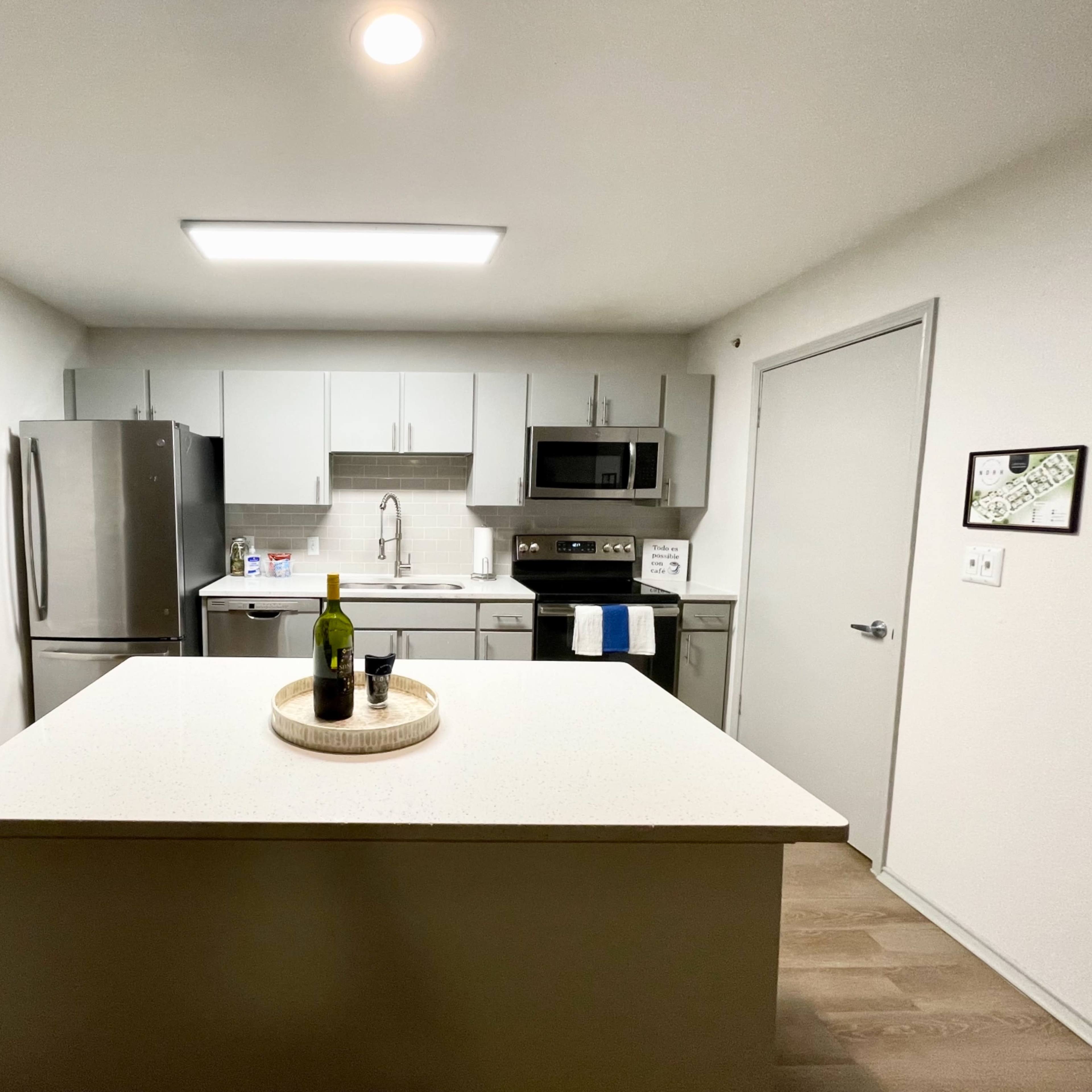 A modern kitchen featuring stainless steel appliances, a central island with a wooden tray, and light-colored cabinetry.