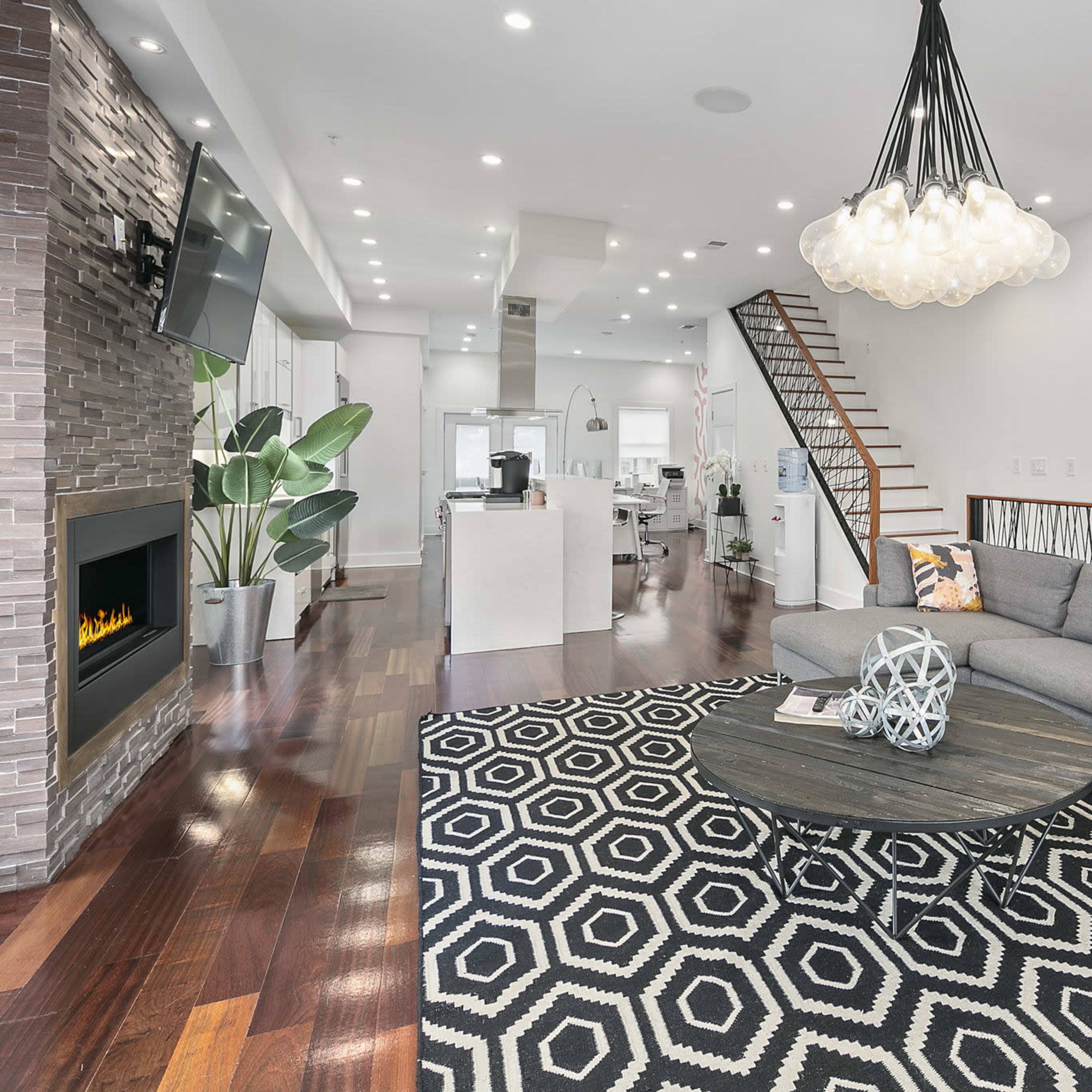 A modern living room featuring a gray sectional sofa, a round coffee table, a patterned rug, and a staircase leading to an upper level.