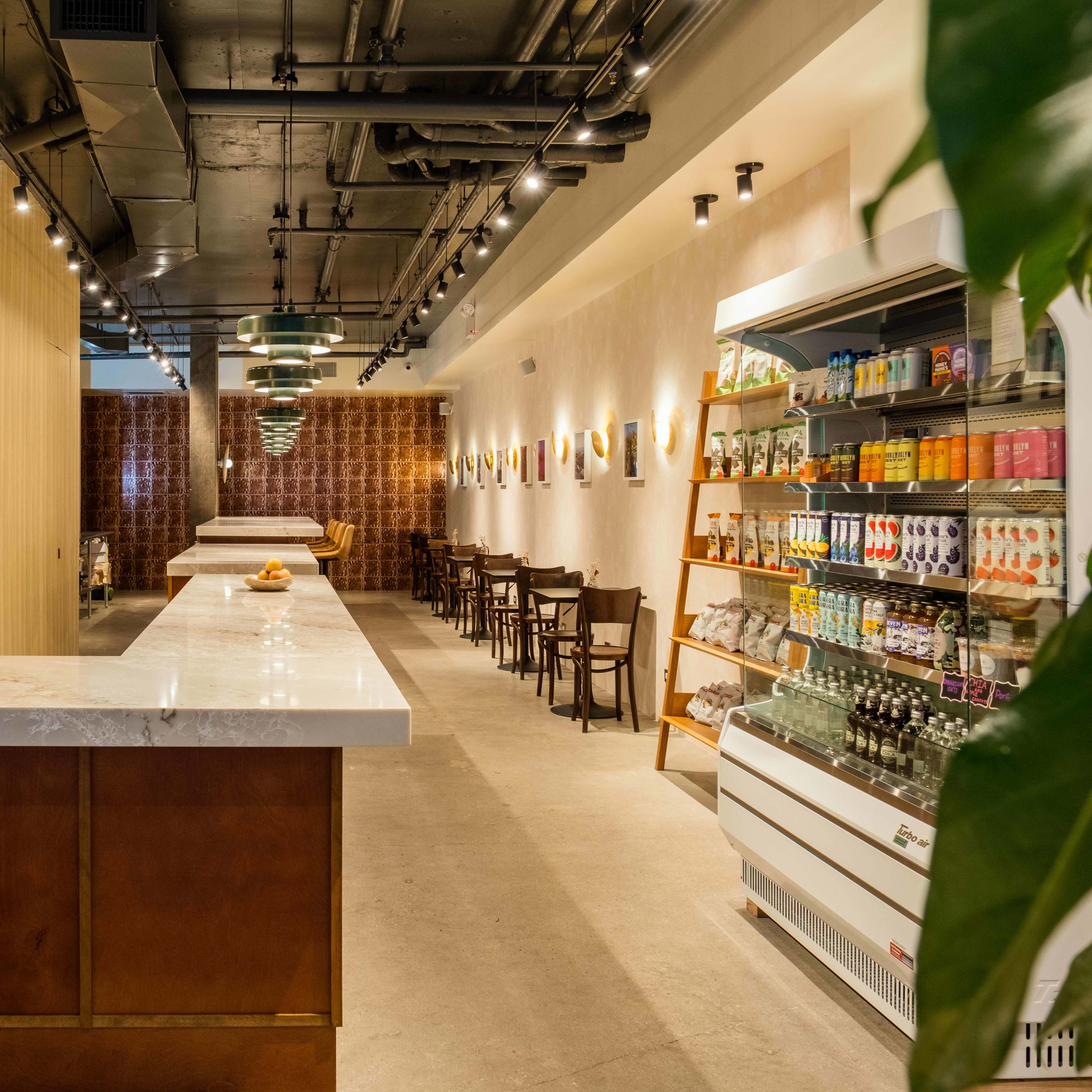 A modern cafe interior featuring a long, empty counter with seating on one side and shelves displaying beverages and snacks on the other.