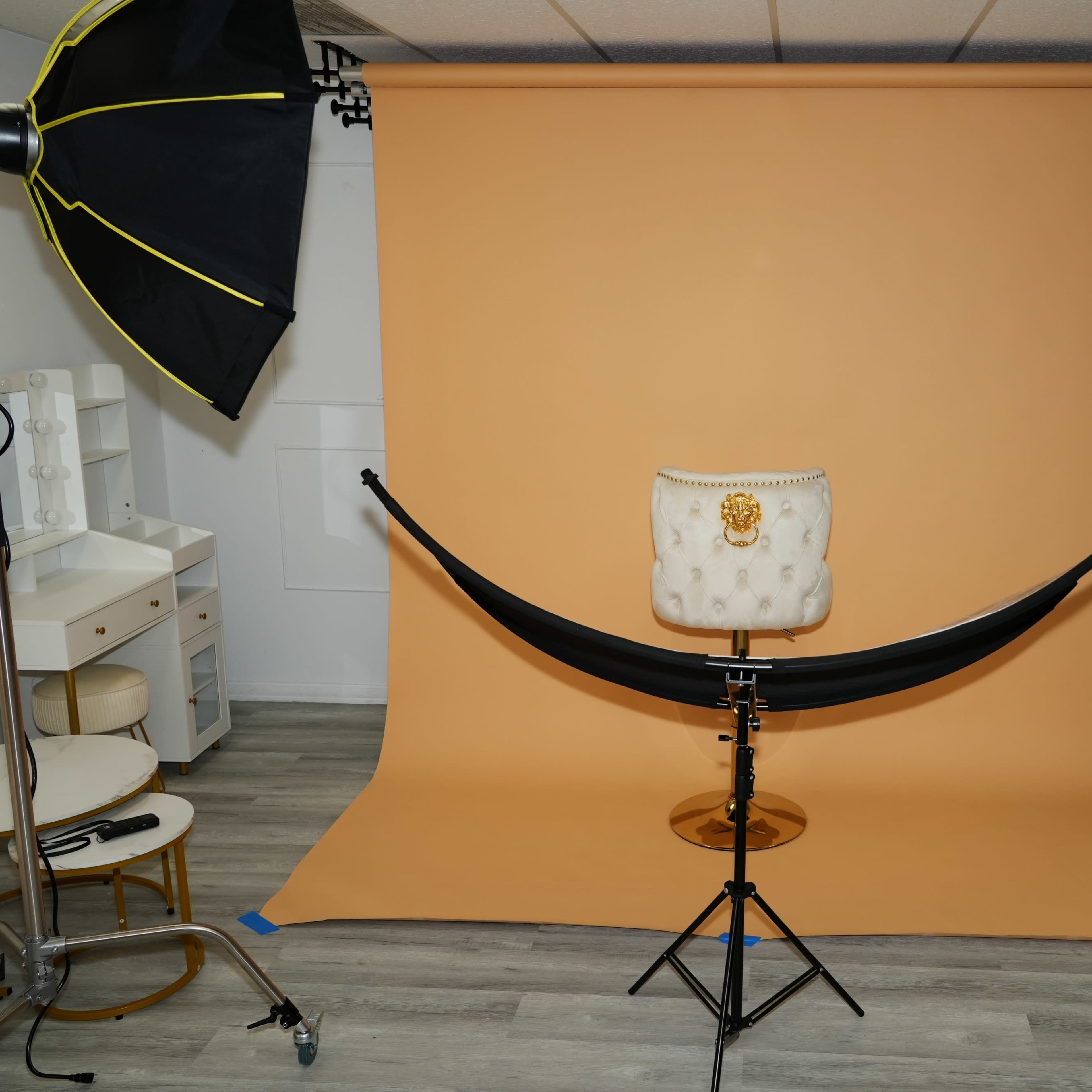 A photography studio setup with a light brown backdrop, a chair in the center, and studio lights positioned on either side.