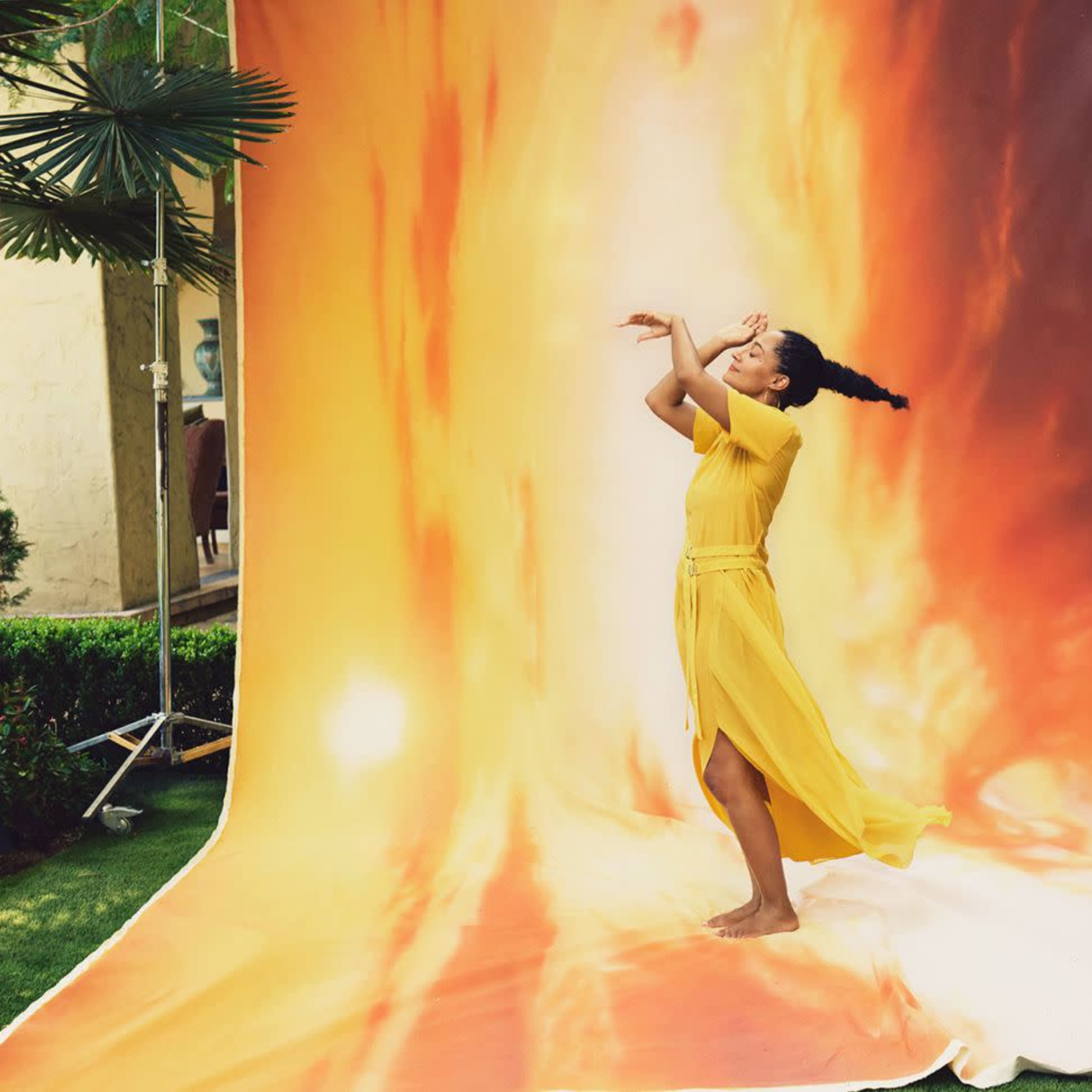 A woman in a yellow dress dances in front of a large, colorful backdrop featuring a sunset.