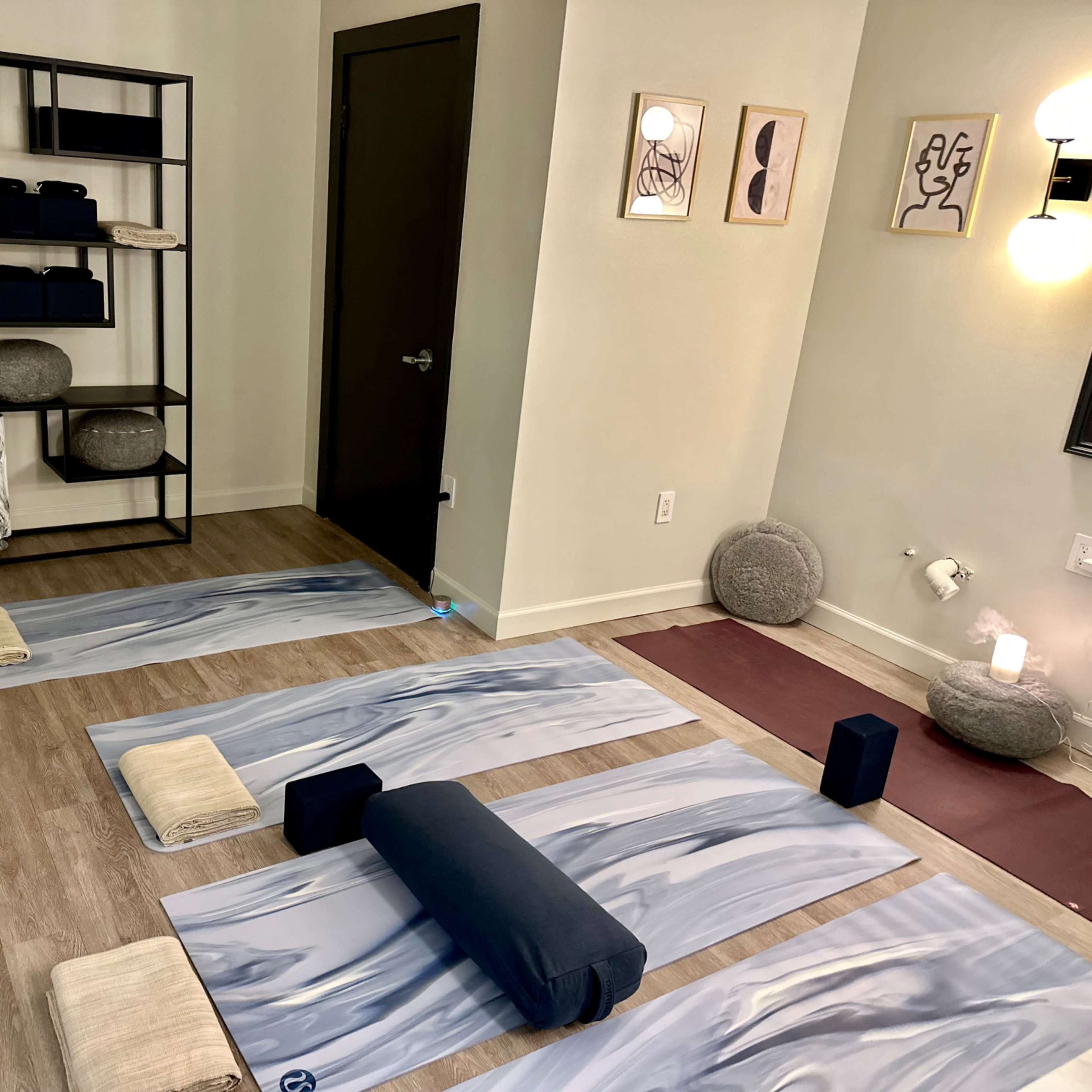 A calm, organized yoga studio with several mats, props, and shelves against a light-colored wall.