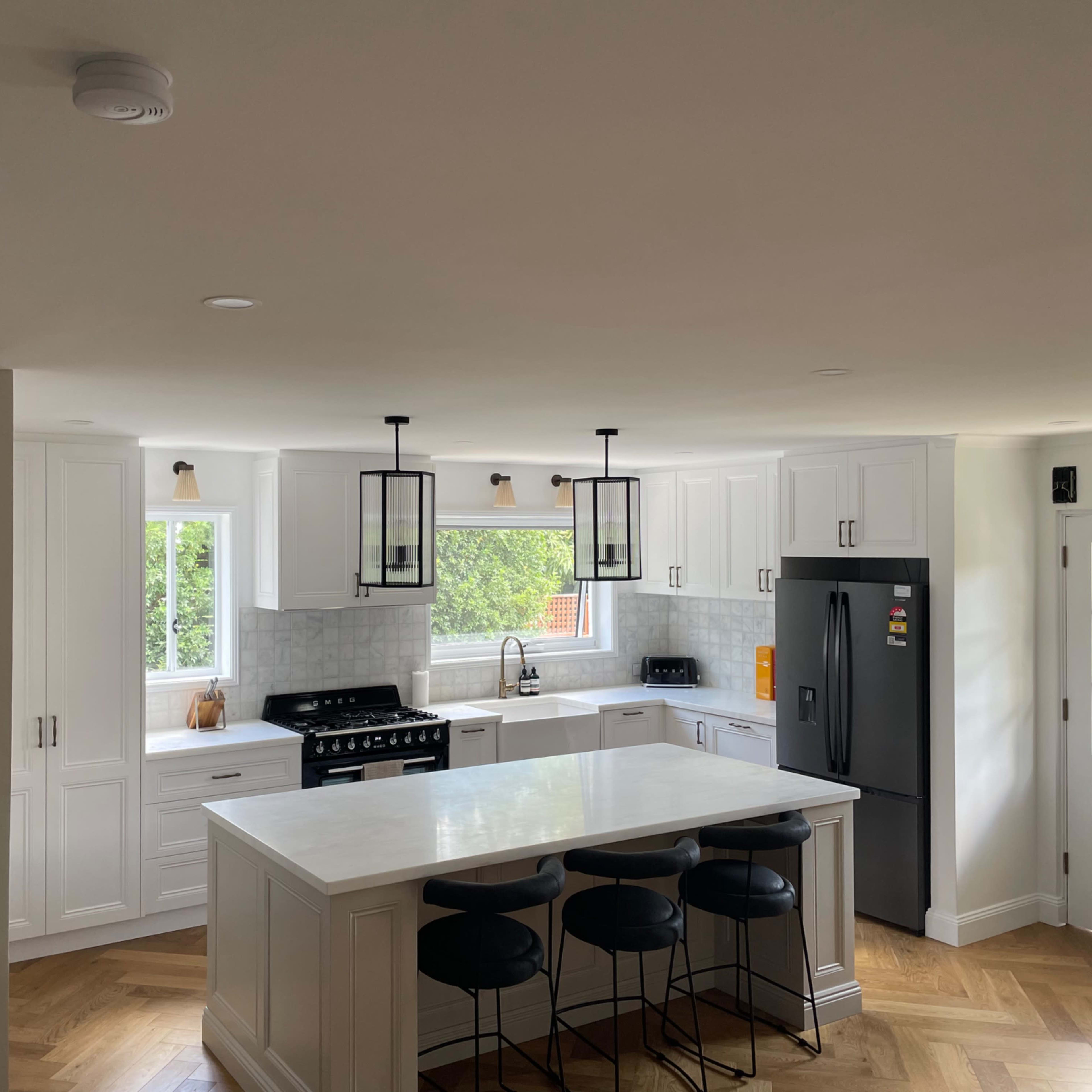 A modern kitchen featuring white cabinetry, a central island with bar stools, and large windows that provide natural light.