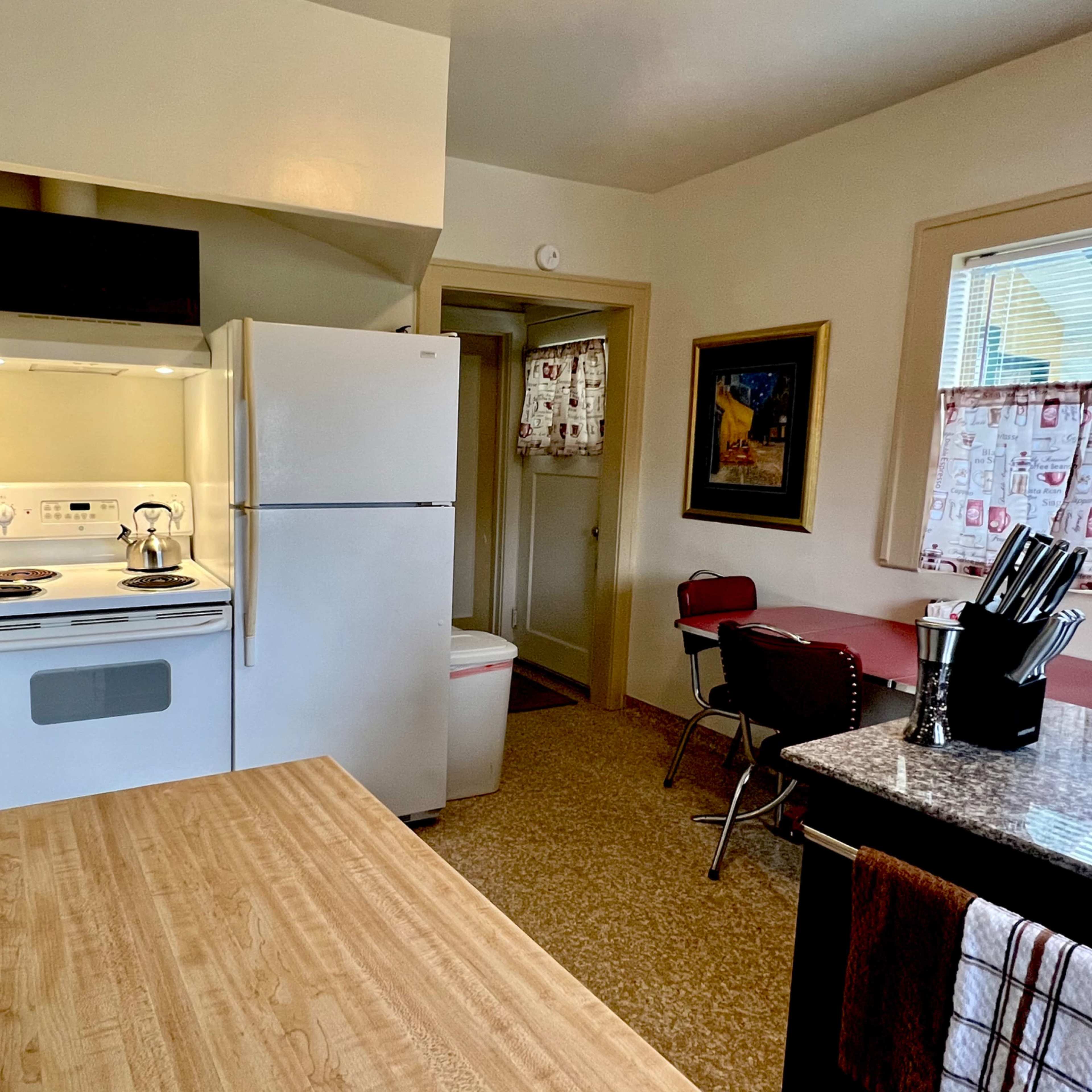 A compact kitchen featuring a stove, refrigerator, and dining area with a small table and chairs.